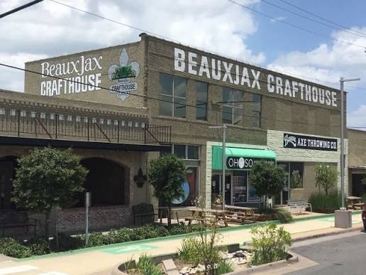 Front view of Beaux Jax Craft House with outdoor seating, trees, and signage on the building.