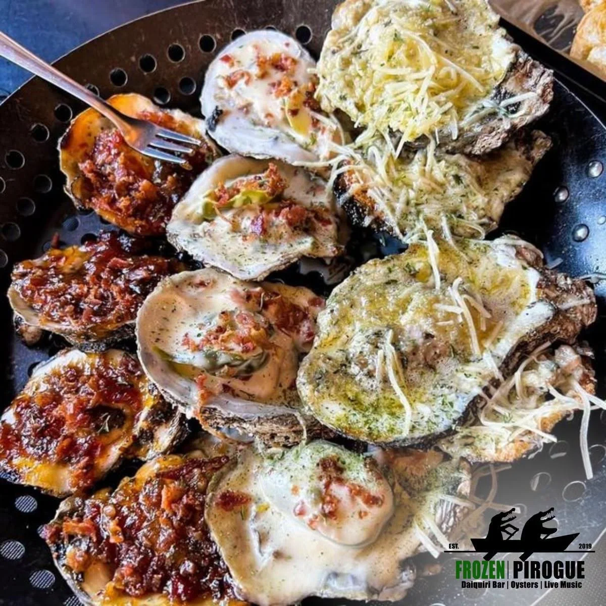 A variety of stuffed oysters on a grill, topped with cheese, herbs, and sauces, served with a fork, with a logo for Frozen Pirogue at the bottom right corner.