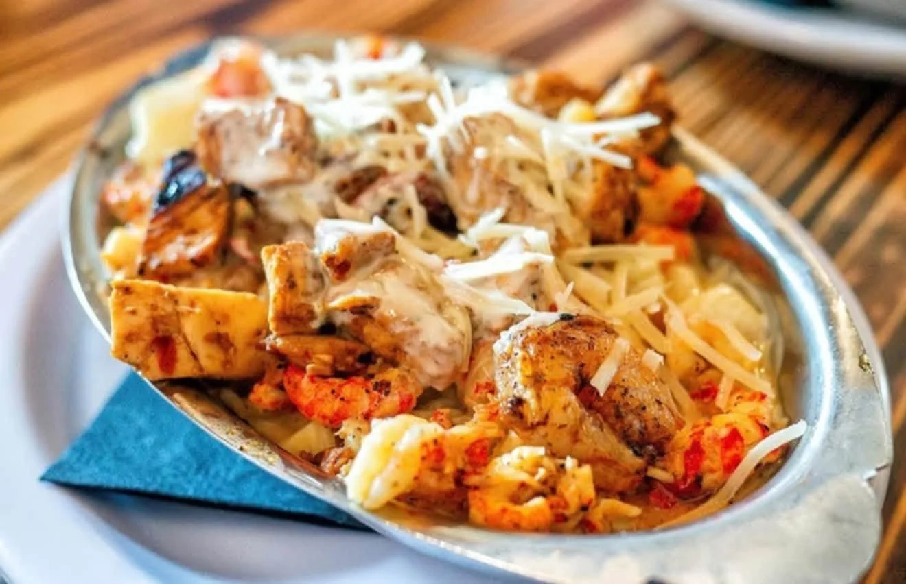A close-up of a sizzling skillet filled with chicken fajitas topped with shredded cheese and served on a plate.