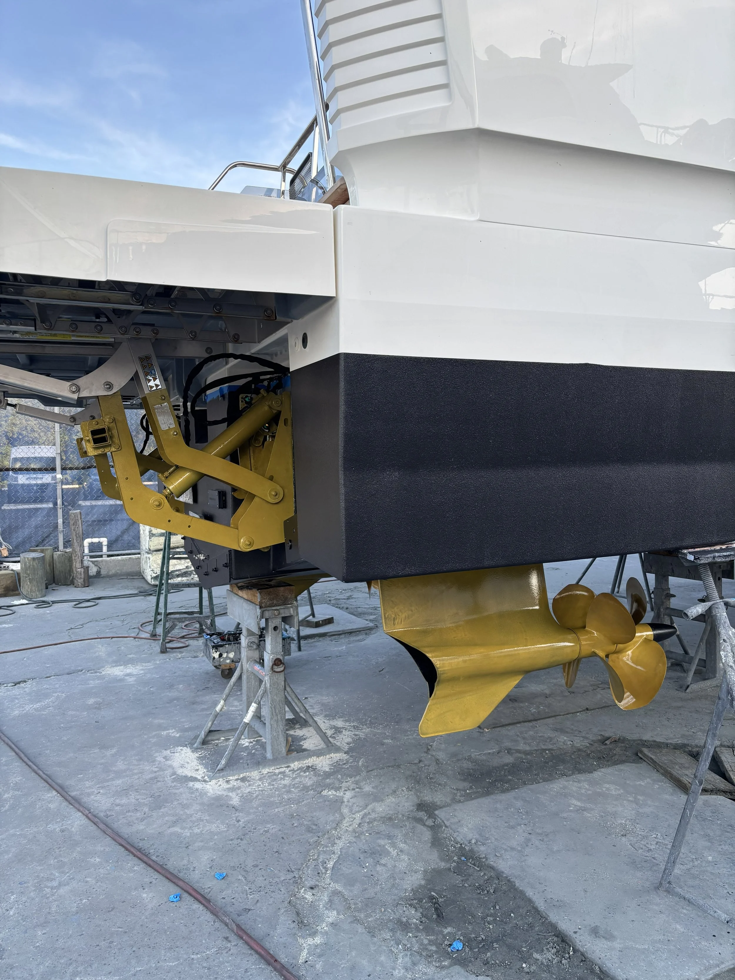 Close-up of a boat propeller and lower hull, showing a black and white hull and a yellow propeller, on a trailer at a boatyard.