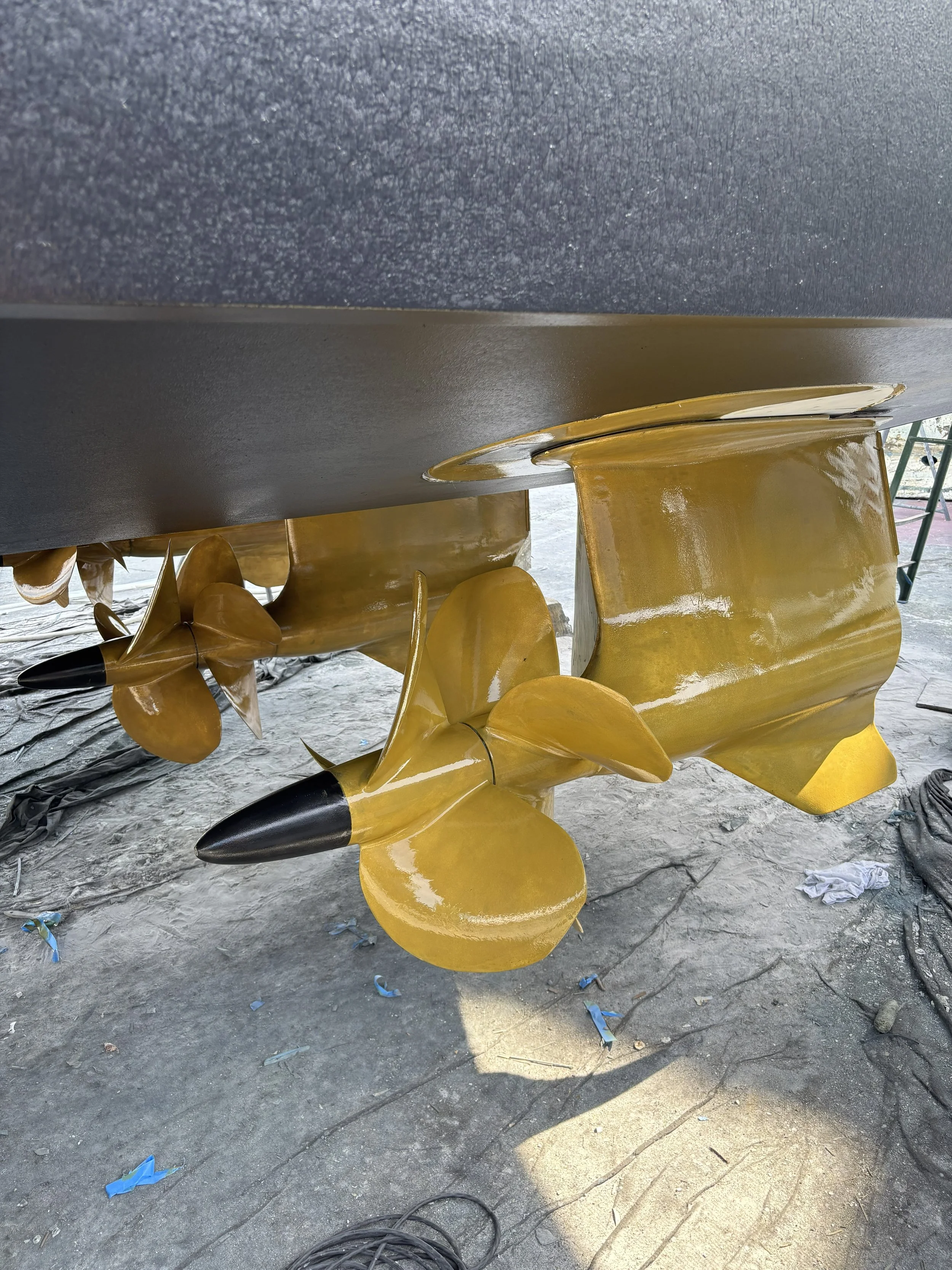 Underwater view of a gold and black propeller with a yellow mounting hub, laying on a dusty surface with some scattered debris around.