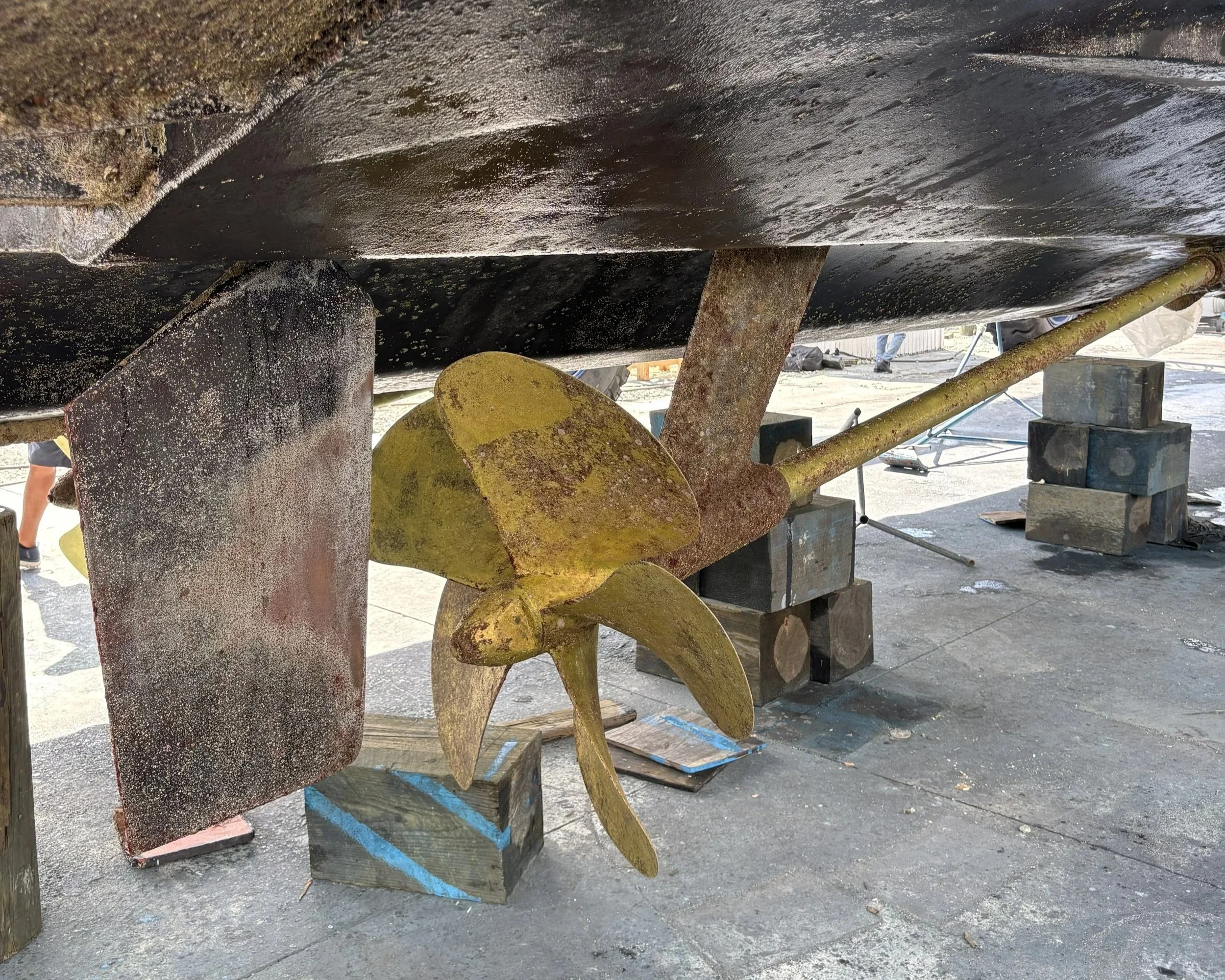 Foundation of a boat on blocks with scaffolding and construction site in background.