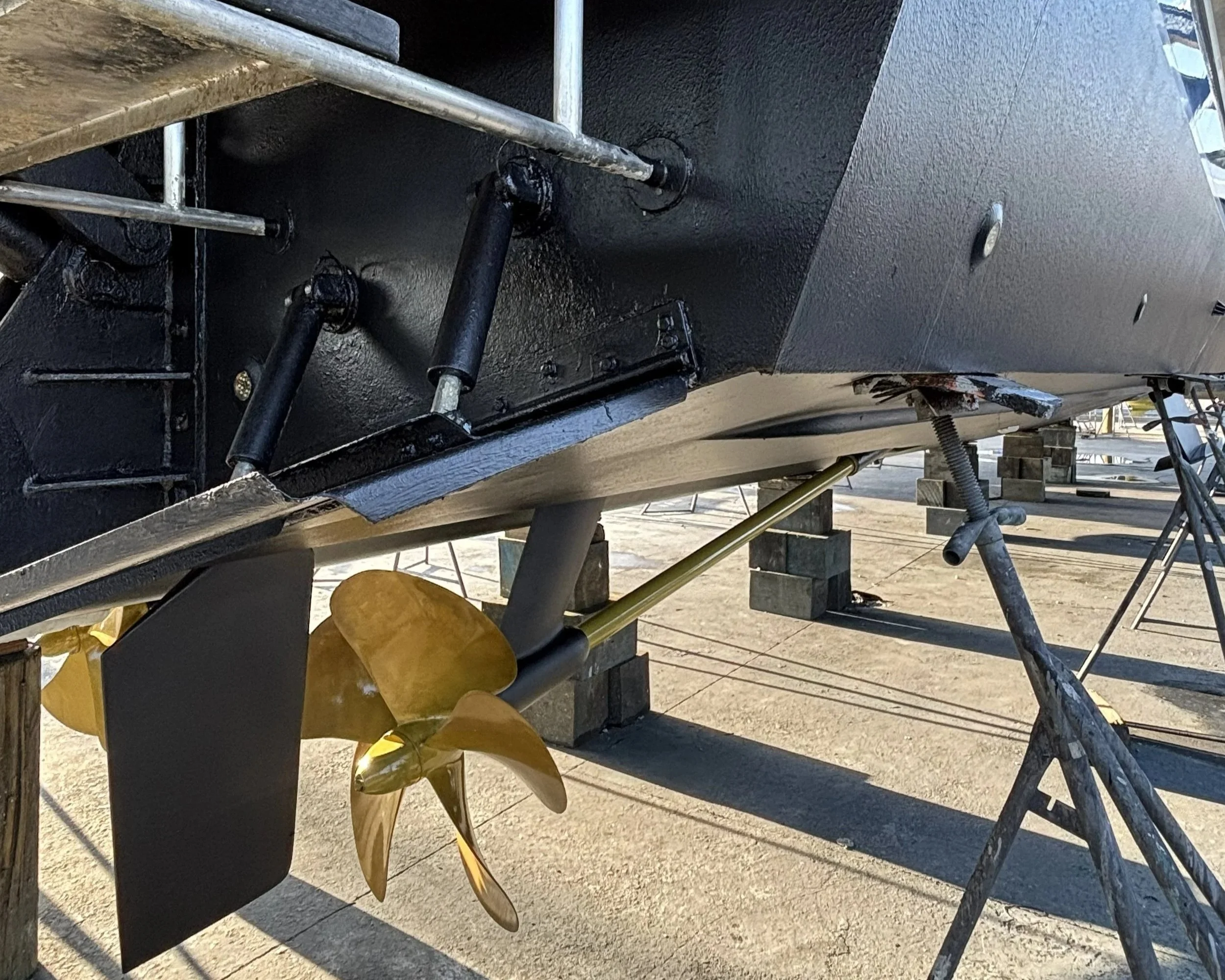 A boat propeller and part of the boat's hull seen upside down on a boat stand outdoors.