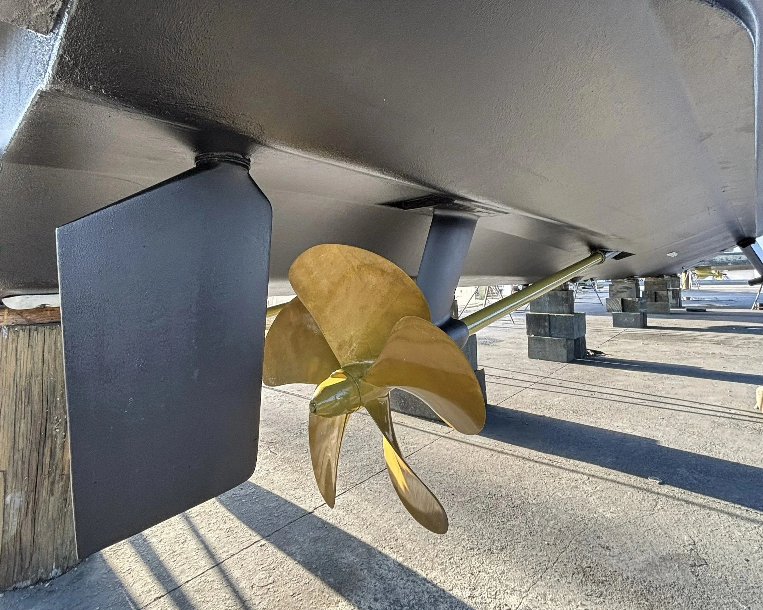 Close-up of a boat's propeller and lower hull, with a wooden post on the left and blocks supporting the boat underneath.