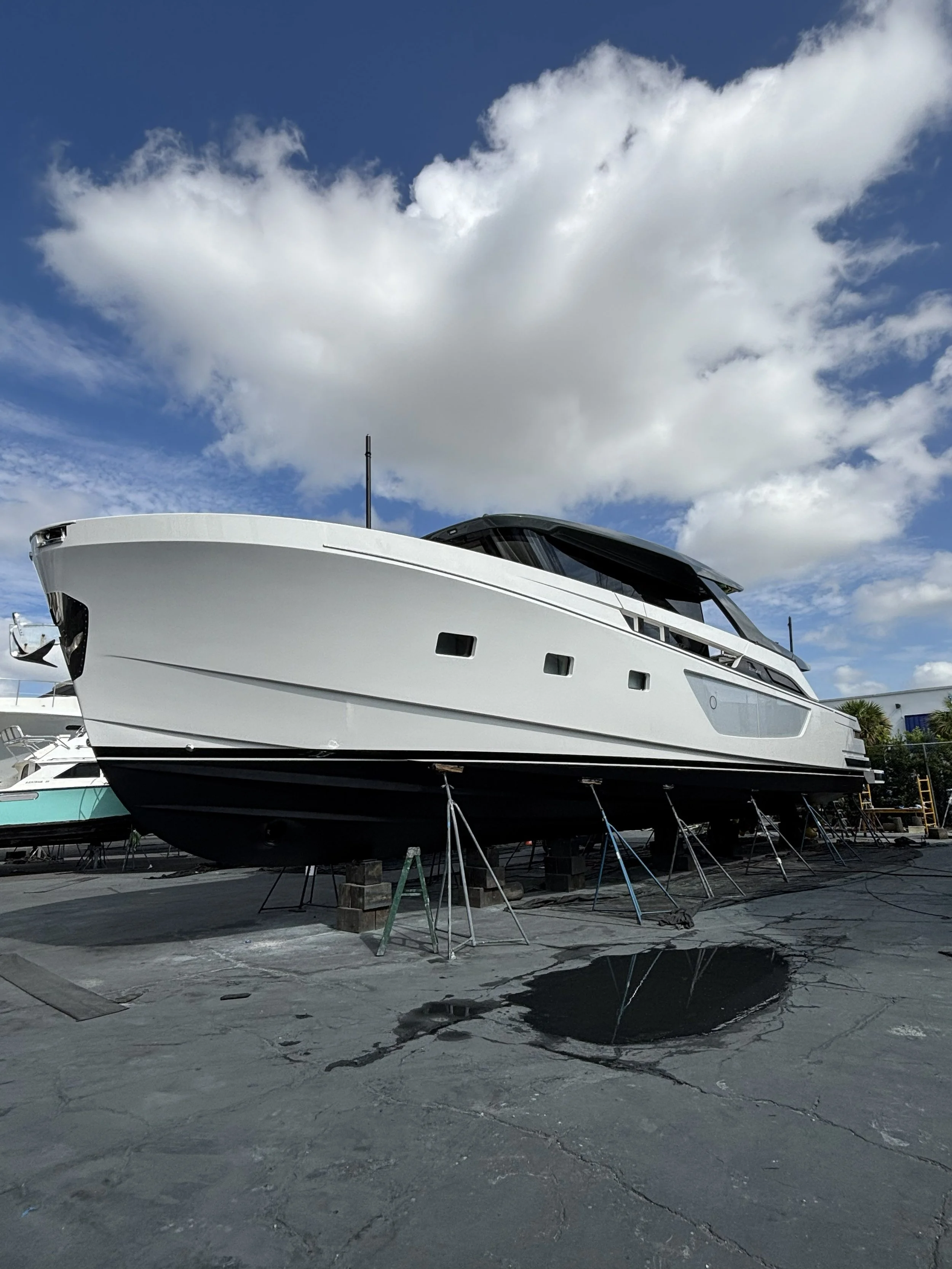 A large white yacht on a boatyard stand, with a blue sky and white clouds above.