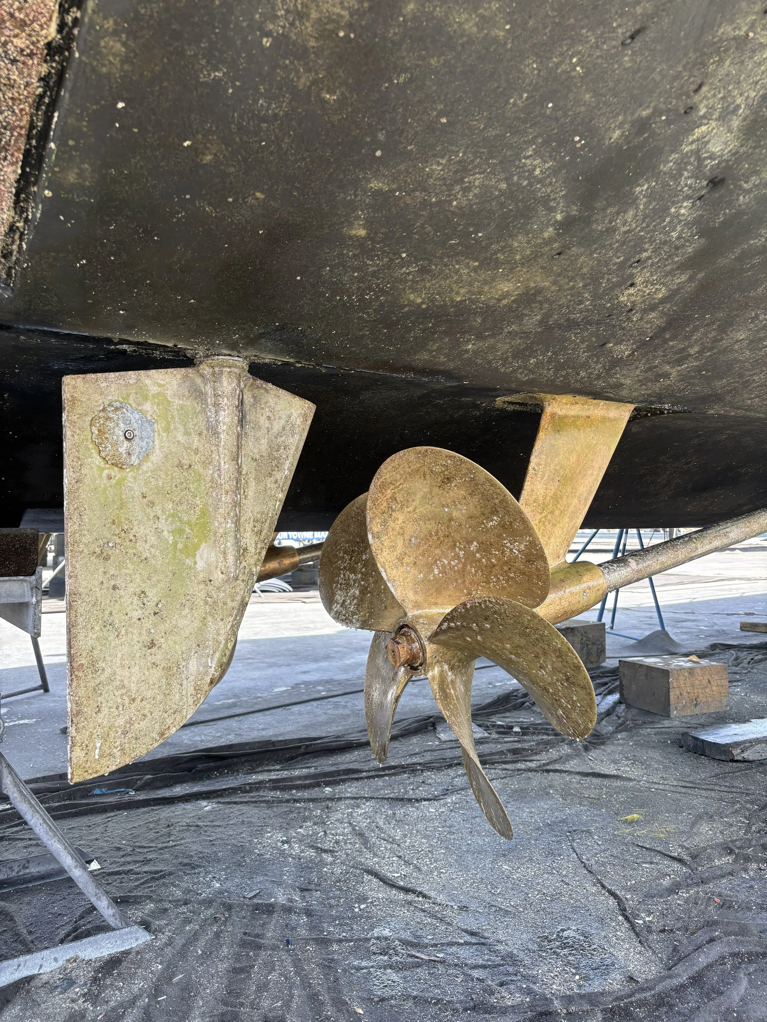 Close-up of the underside of a boat showing its propeller, with boat supports and concrete floor beneath.