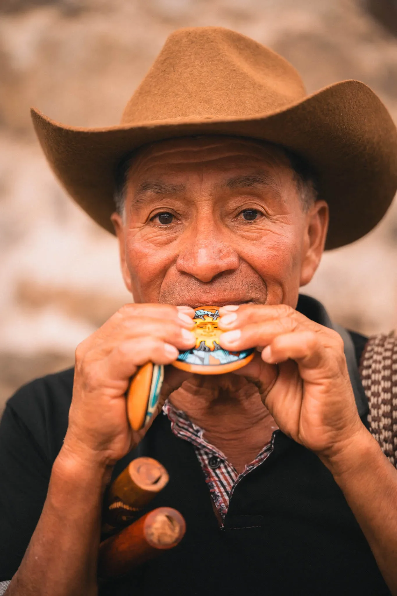 An elderly man wearing a brown cowboy hat playing with a small colorful toy. The background is blurred.