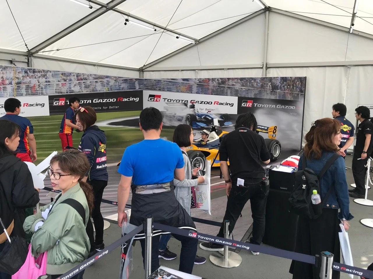 Visitors gather and take photos at an event booth with a racing car illusion