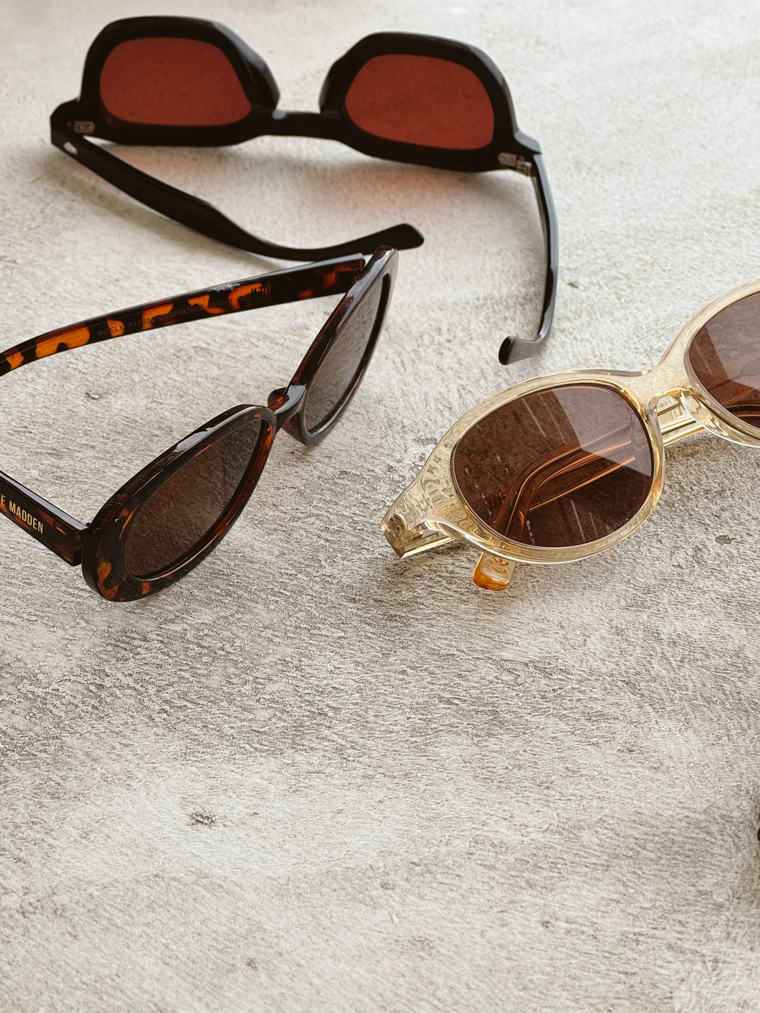 Three pairs of sunglasses on a light-colored textured surface.