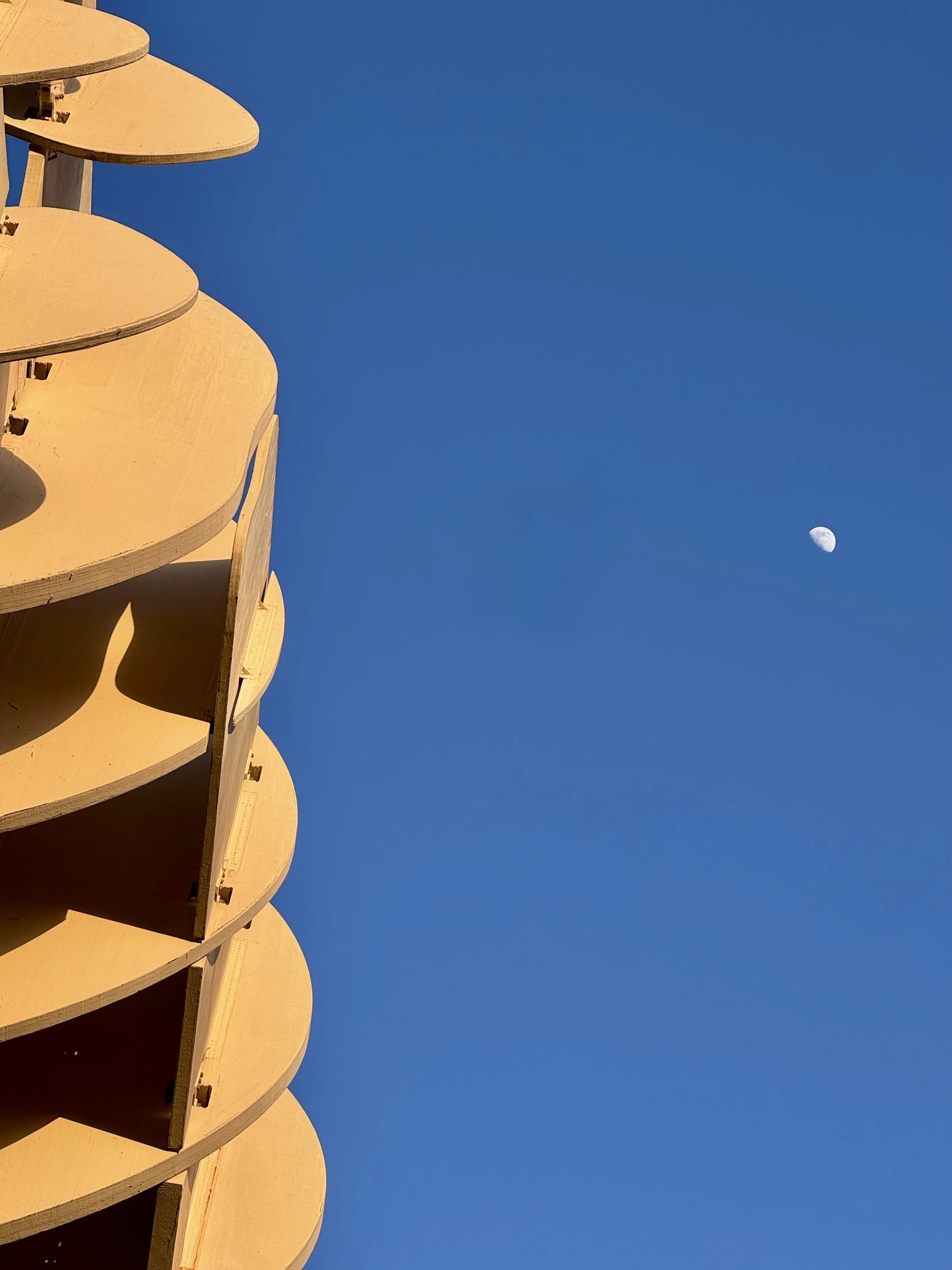 A building with multiple circular balconies painted in a light color, set against a clear blue sky with a visible waxing gibbous moon.