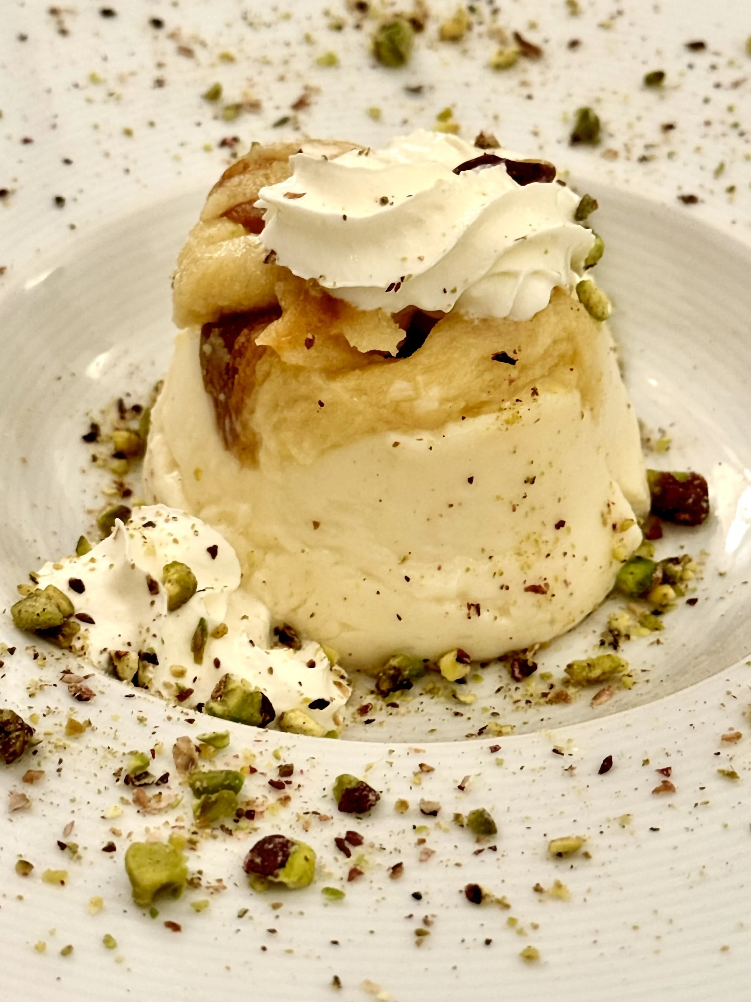 A scoop of vanilla ice cream garnished with whipped cream, crushed pistachios, and chocolate shavings.