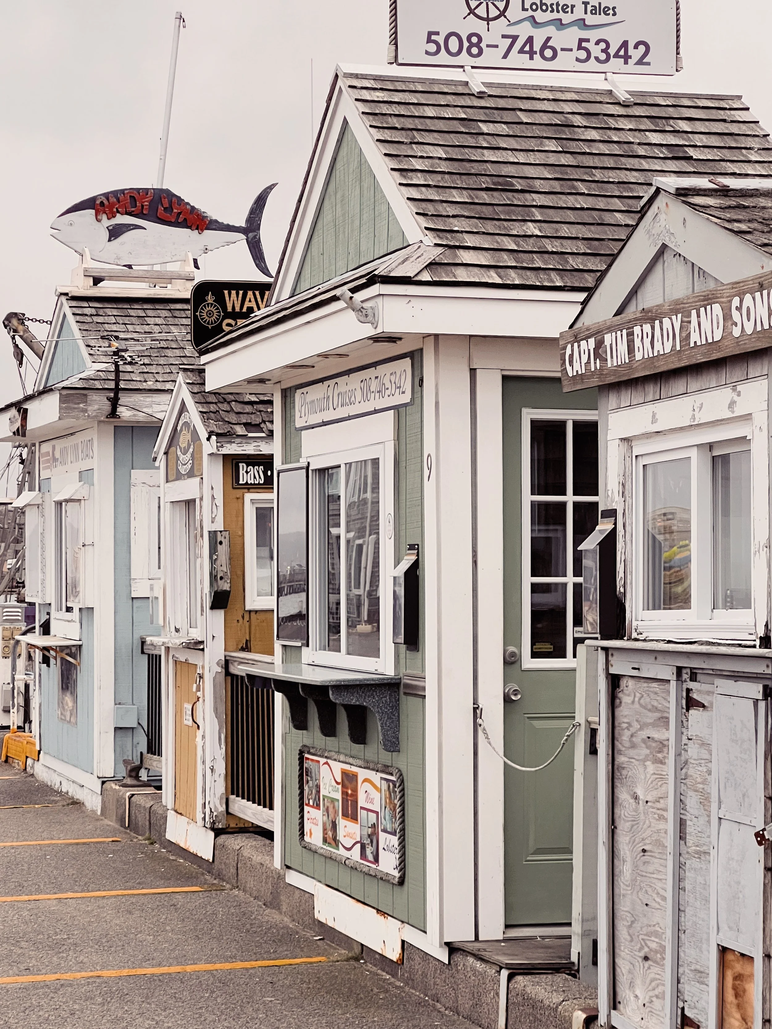 Various small buildings or booths with signs, including a lobster-themed sign on top of one building, located along a parking lot with painted space lines and concrete wheel stops.