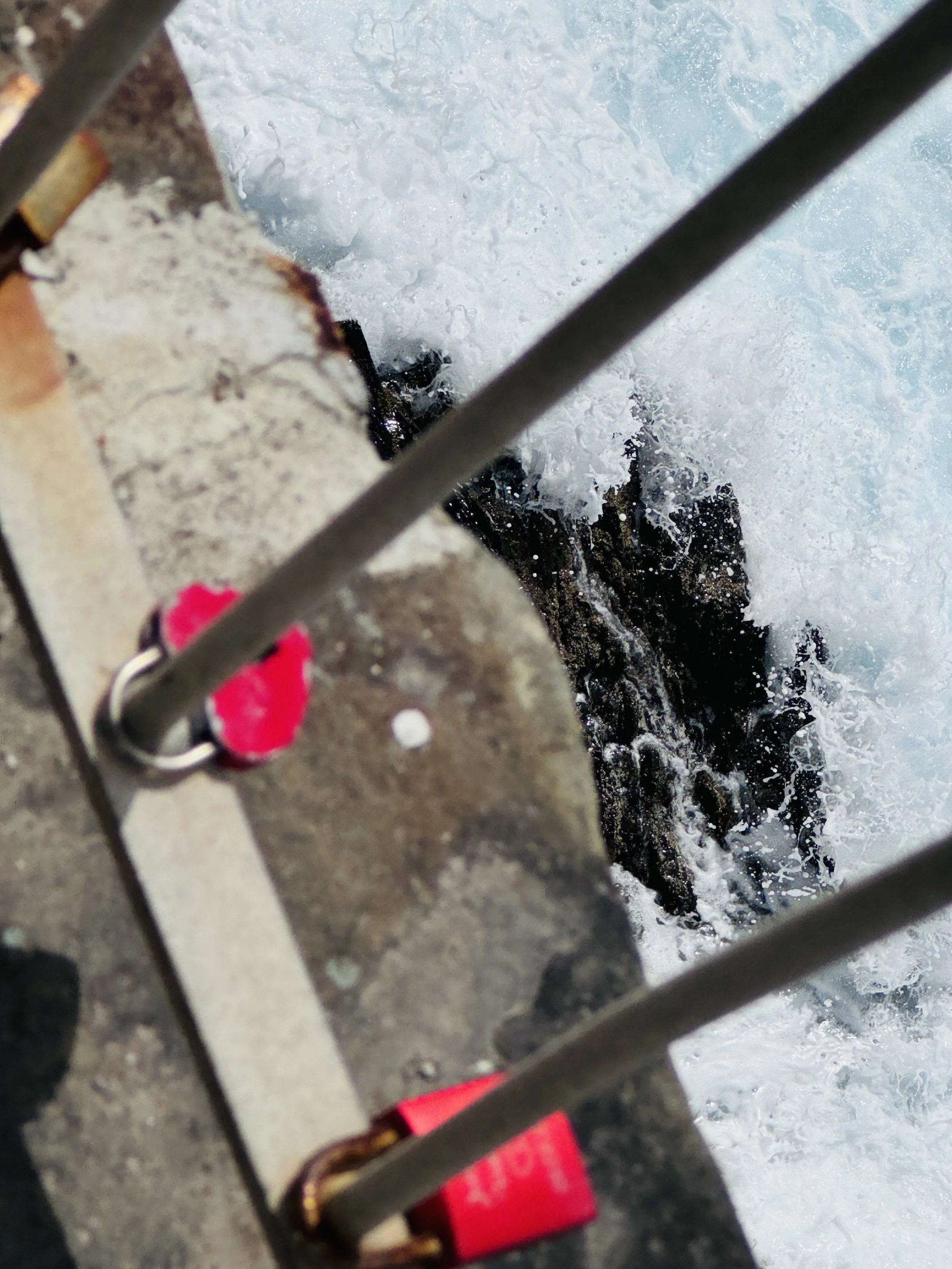 View from a boat showing the water splashing against rocks below, with a metal railing and part of the boat's structure visible in the foreground.