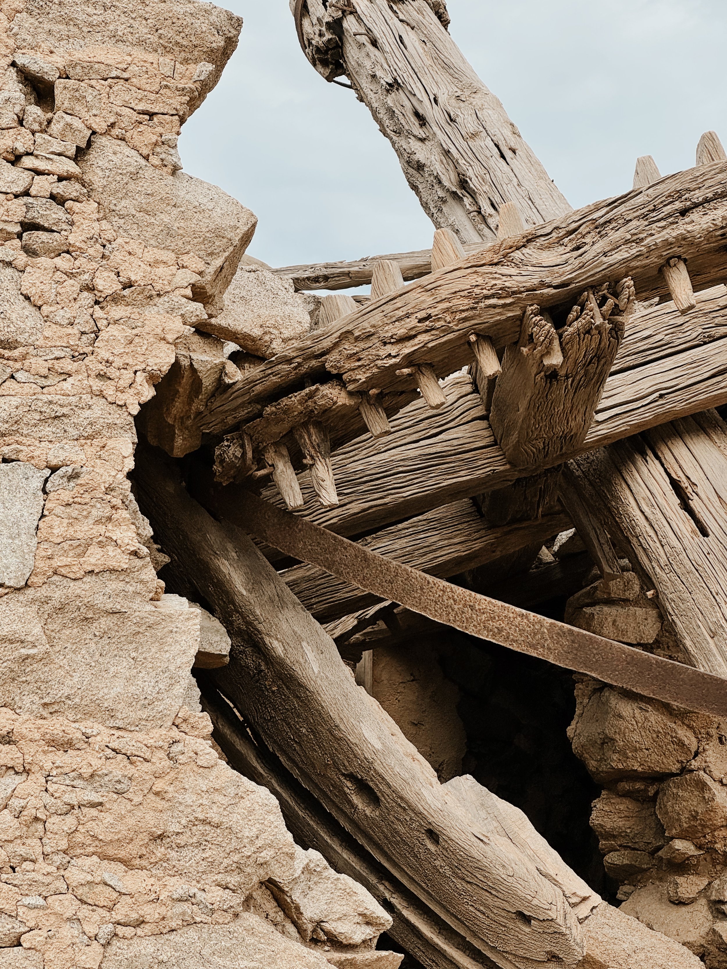 Close-up photo of an old wooden structure with weathered beams, alongside a rough stone wall. The scene appears to be in a rustic or abandoned building.