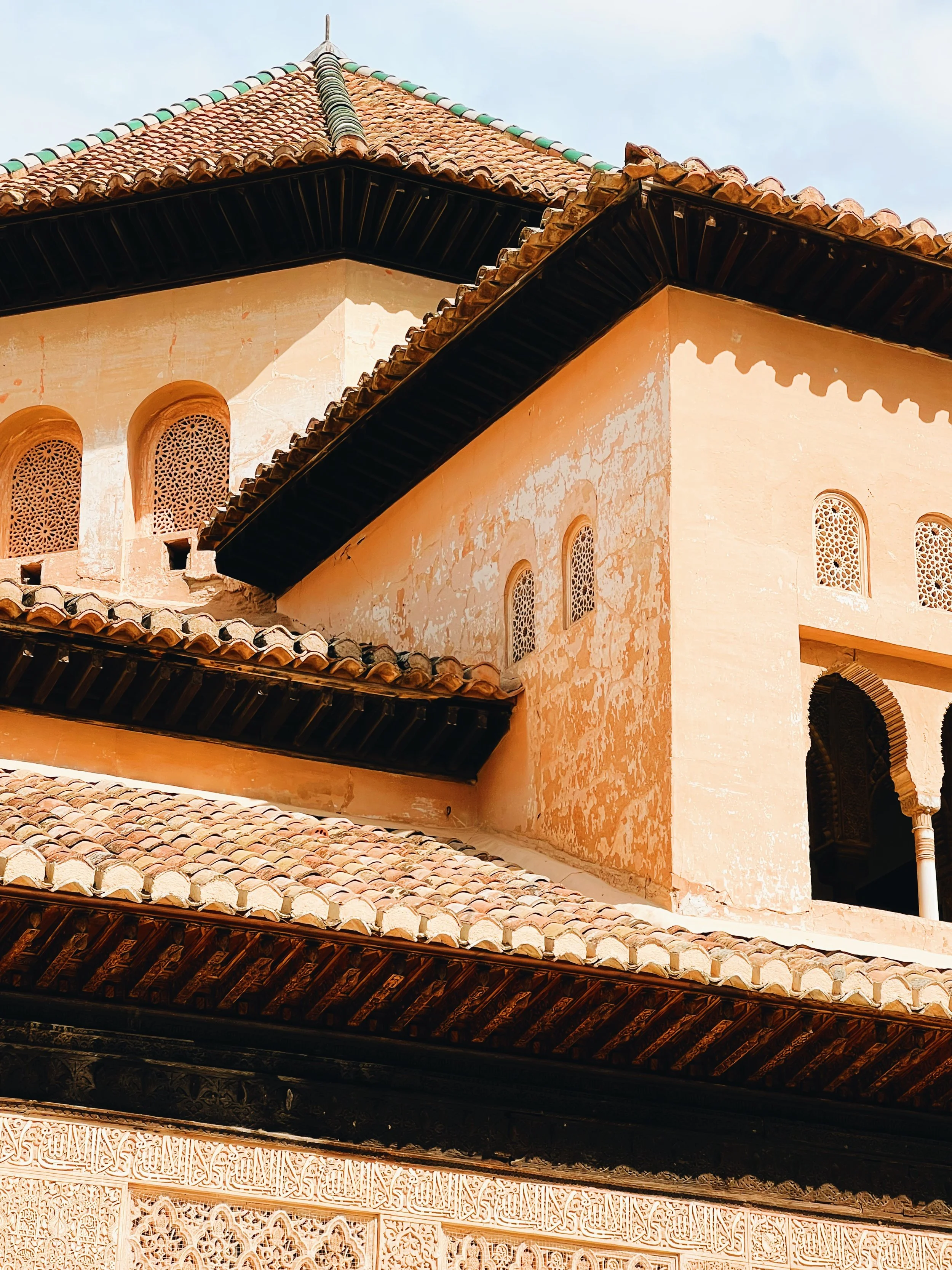 Close-up of a traditional Andalusian building with ornate carvings, intricate wooden latticework, and a terracotta tiled roof under a blue sky.