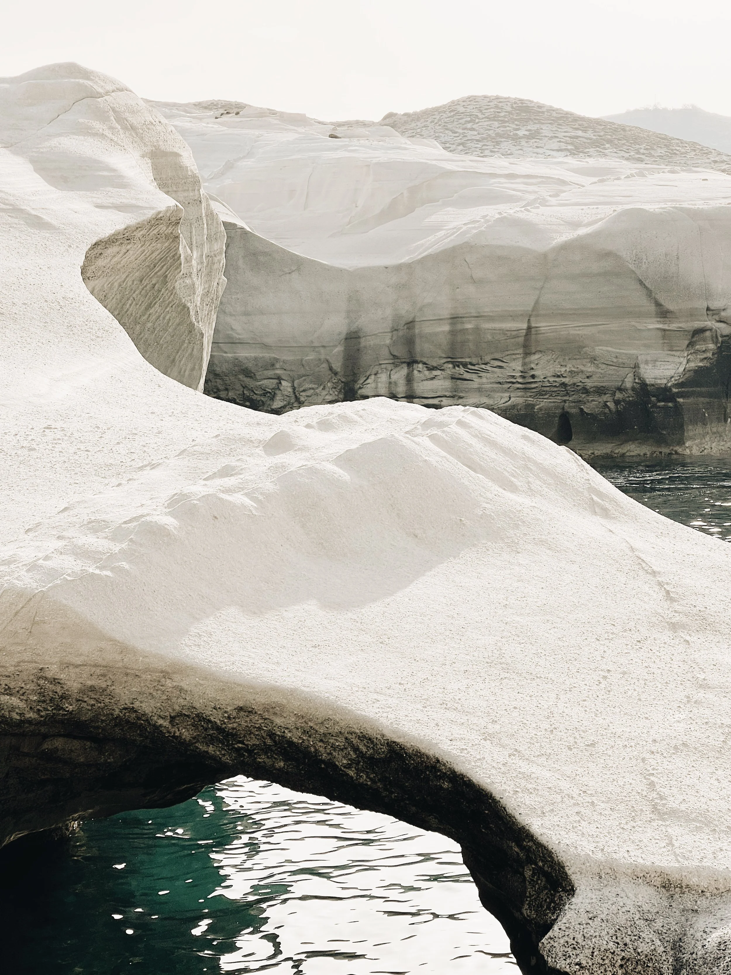 Ice formations with a small body of water at the base, featuring large, textured ice blocks and rocky hills in the background.
