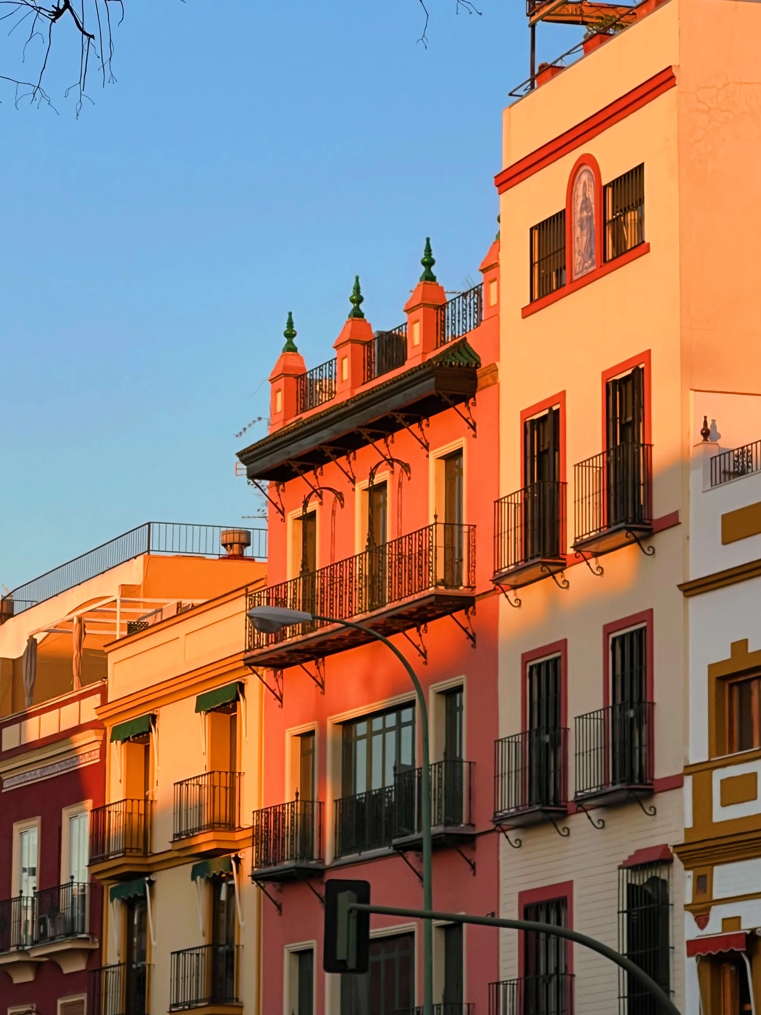 Colorful multi-story buildings with balconies, decorative elements, and a street lamp in front, under a clear blue sky.