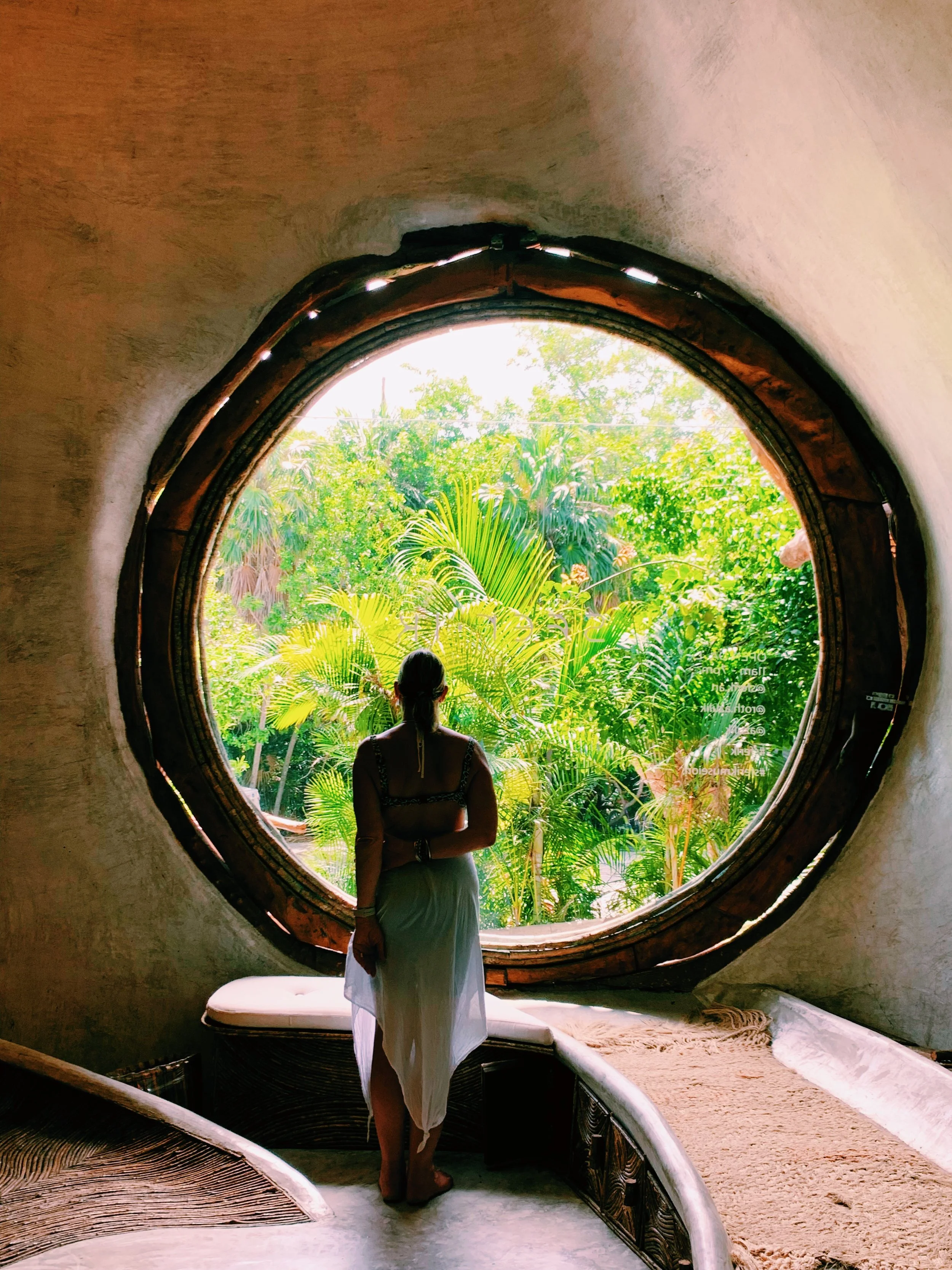 Woman standing inside a rounded opening looking out at lush green tropical plants.
