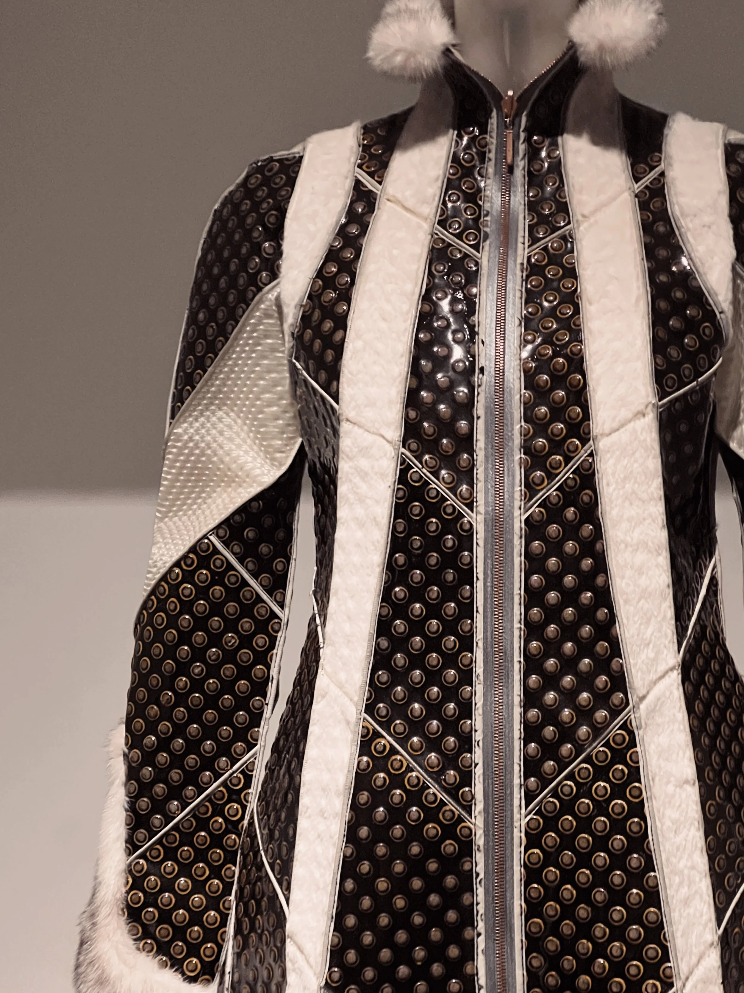 A men's winter jacket with a black and tan polka dot pattern, white fur trim on the front panels, and fluffy white fur at the collar.