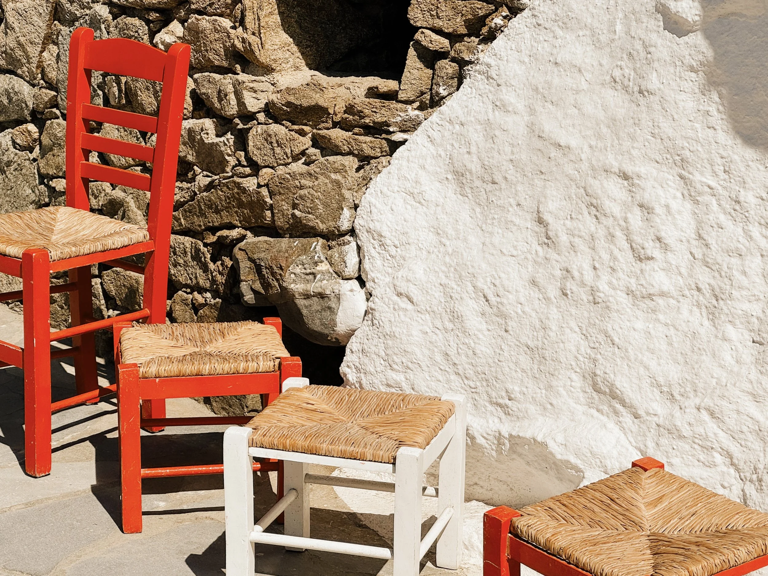 Red and white wooden chairs with woven seats lined up against a stone and white wall.