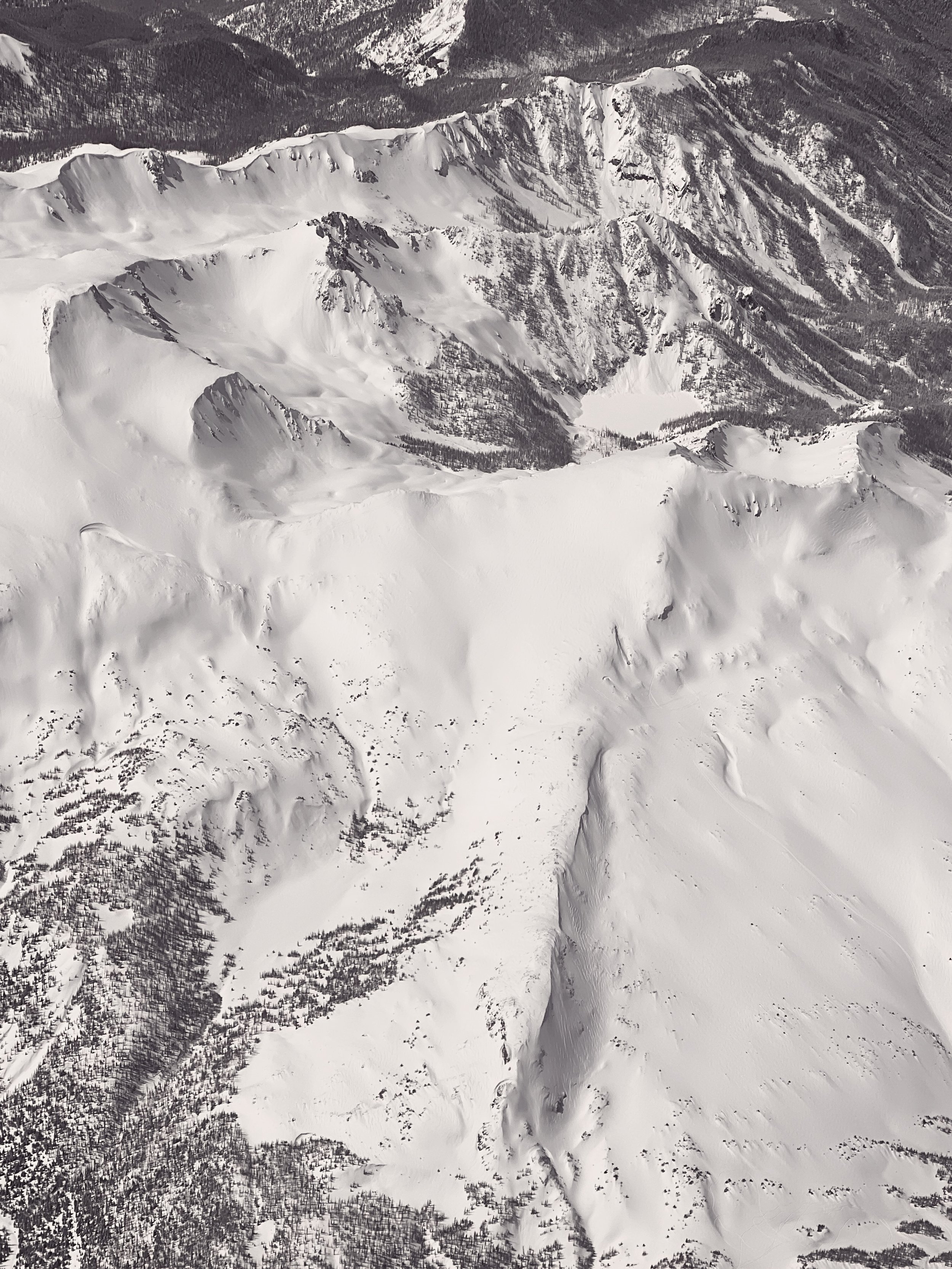 Aerial view of a snow-covered mountain landscape with ridges, valleys, and forests.
