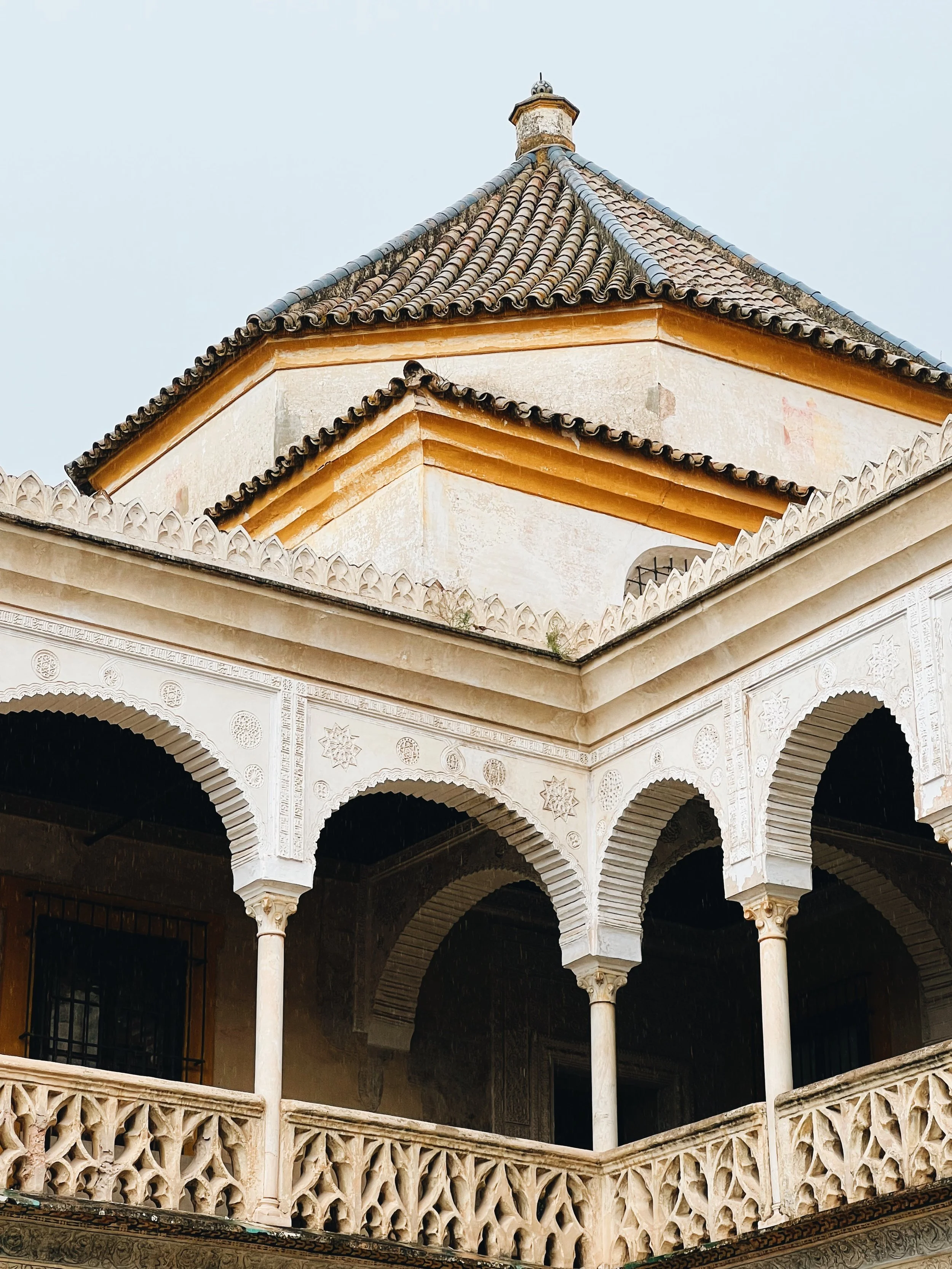 Close-up of intricate architectural details on a historic building, featuring a tiled roof, arched windows, and ornate decorative elements on columns and balconies.