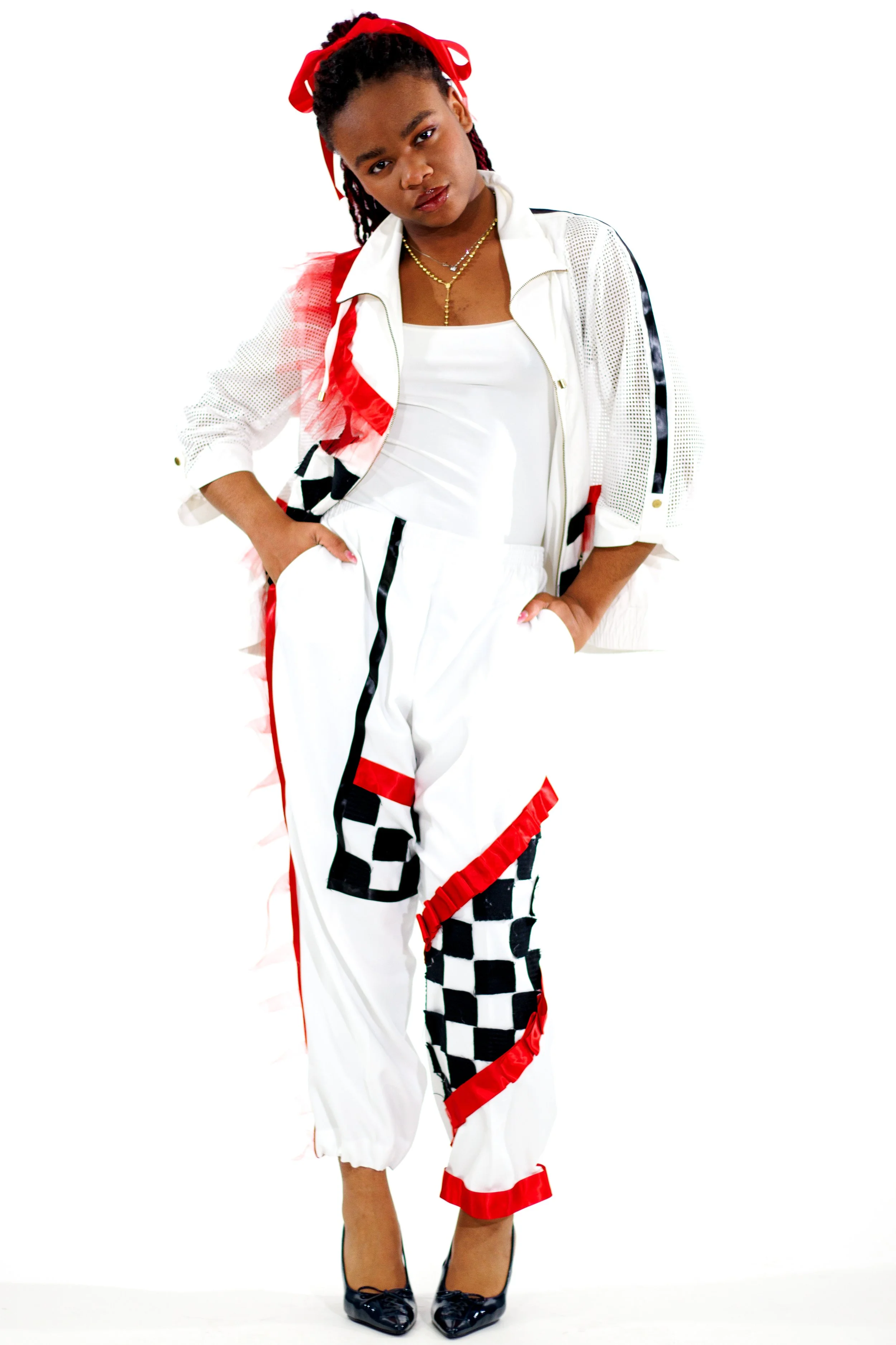 Person wearing a white and red ruffled outfit with a black-and-white checkerboard panel and red headband against a white background