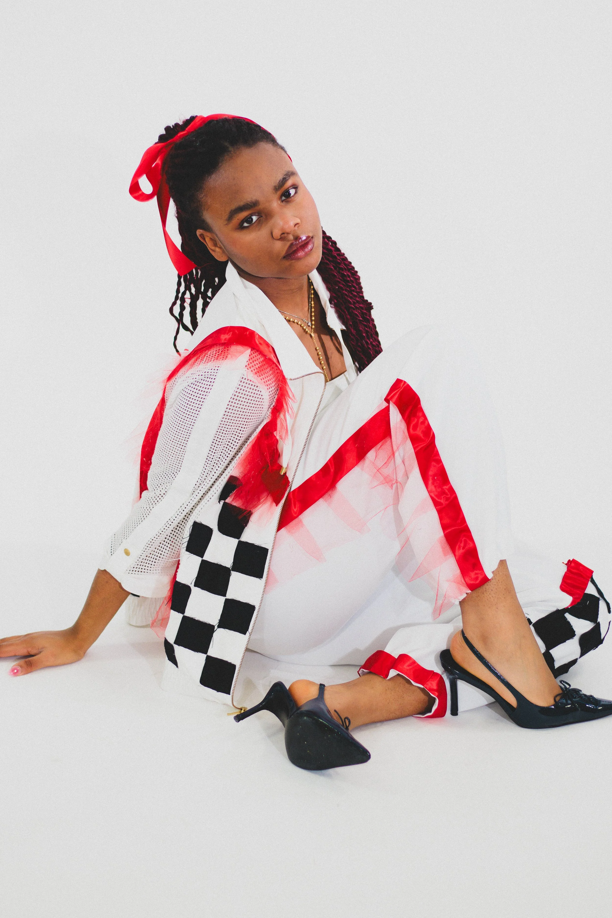 Fashion portrait of a Black woman with braided hair wearing a red headband, white and red outfit, and black high heels.