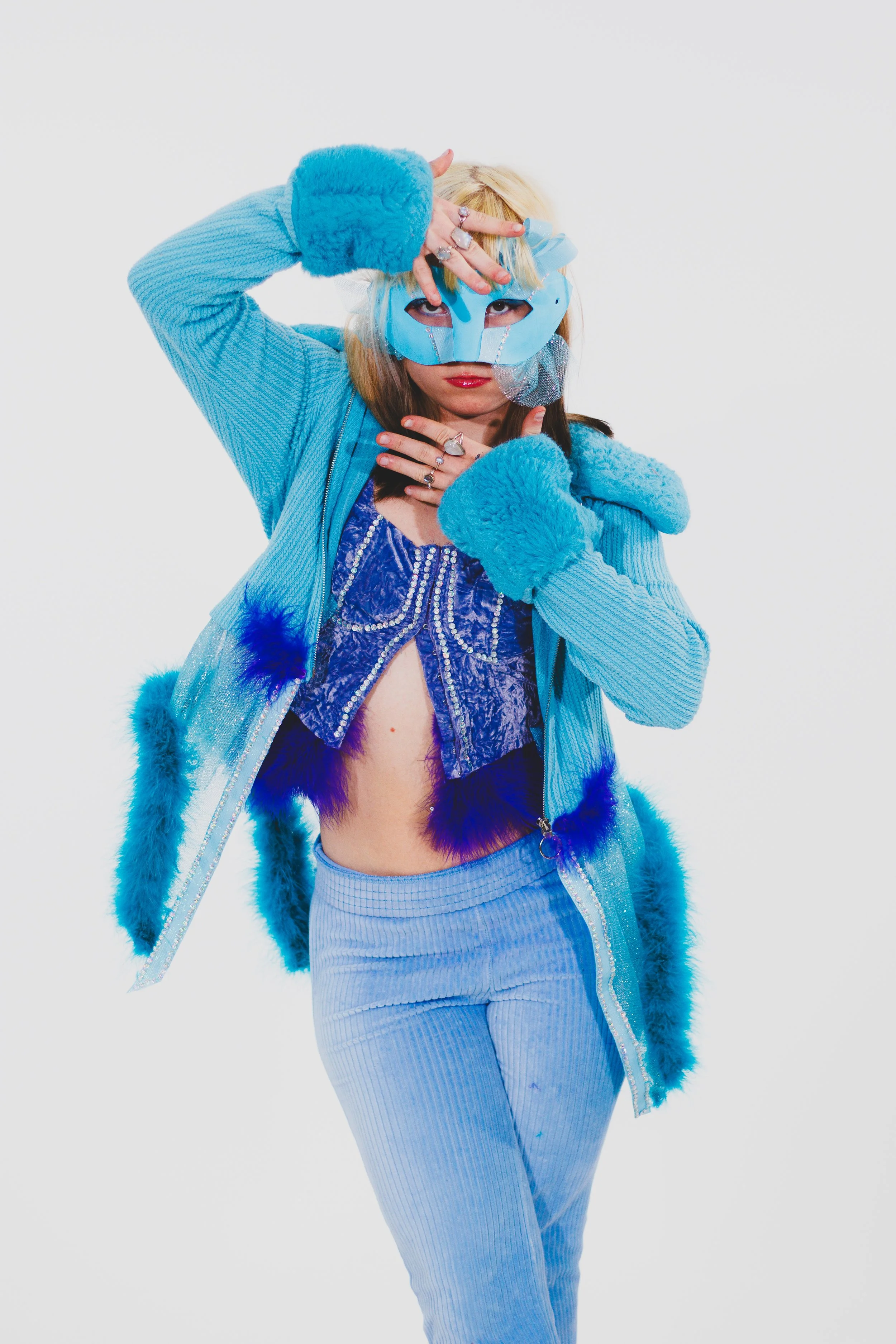 Person in an elaborate blue costume and jeweled mask posing against a white background