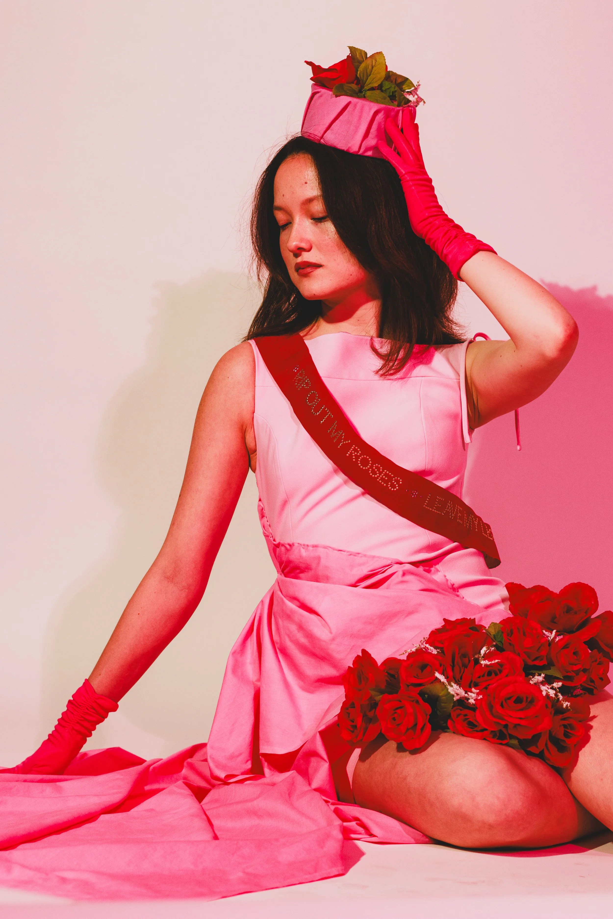 Woman in a pink dress and gloves wearing a flower-covered hat and holding red roses