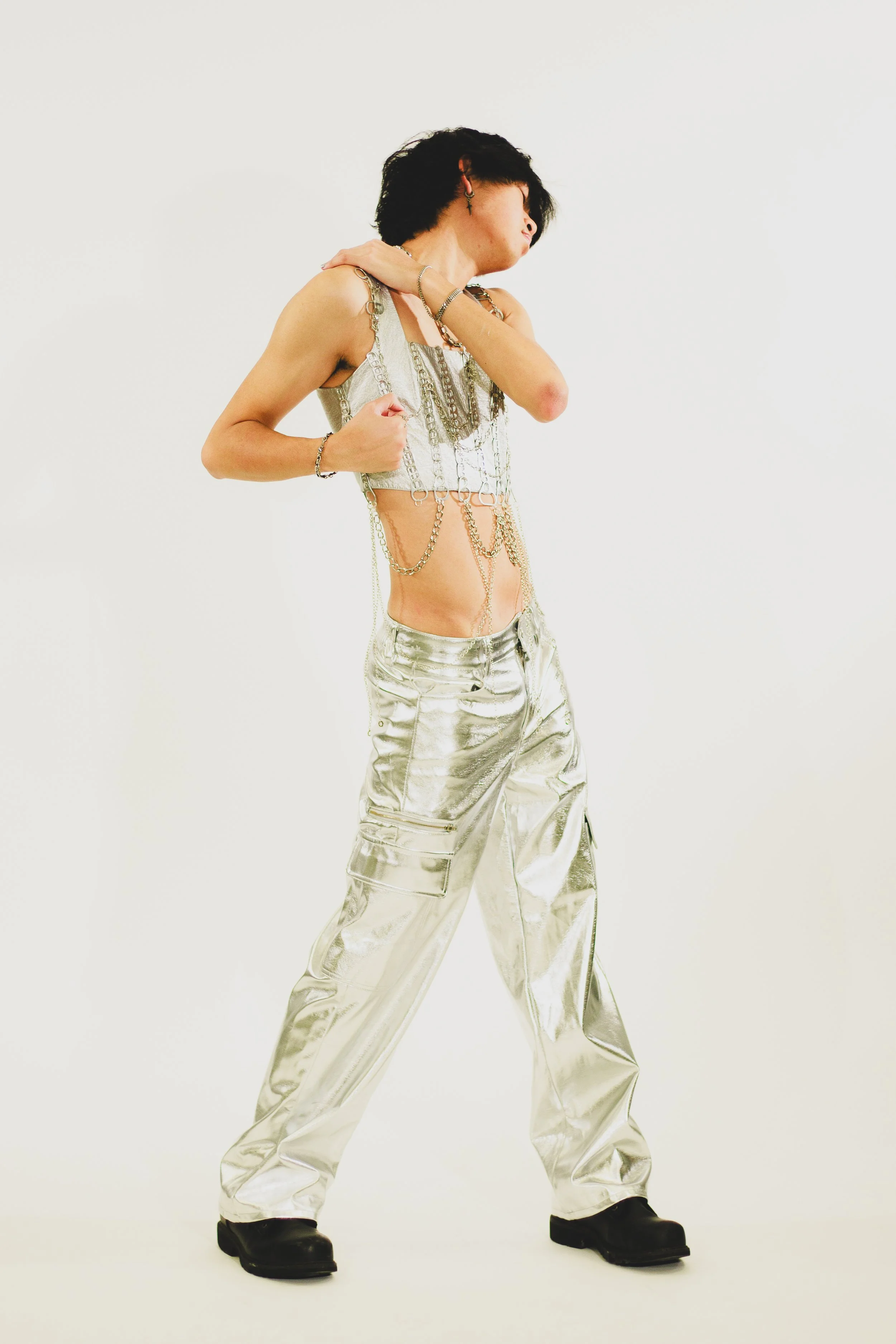 Person in a silver chain-draped cropped top and metallic pants posing against a white background