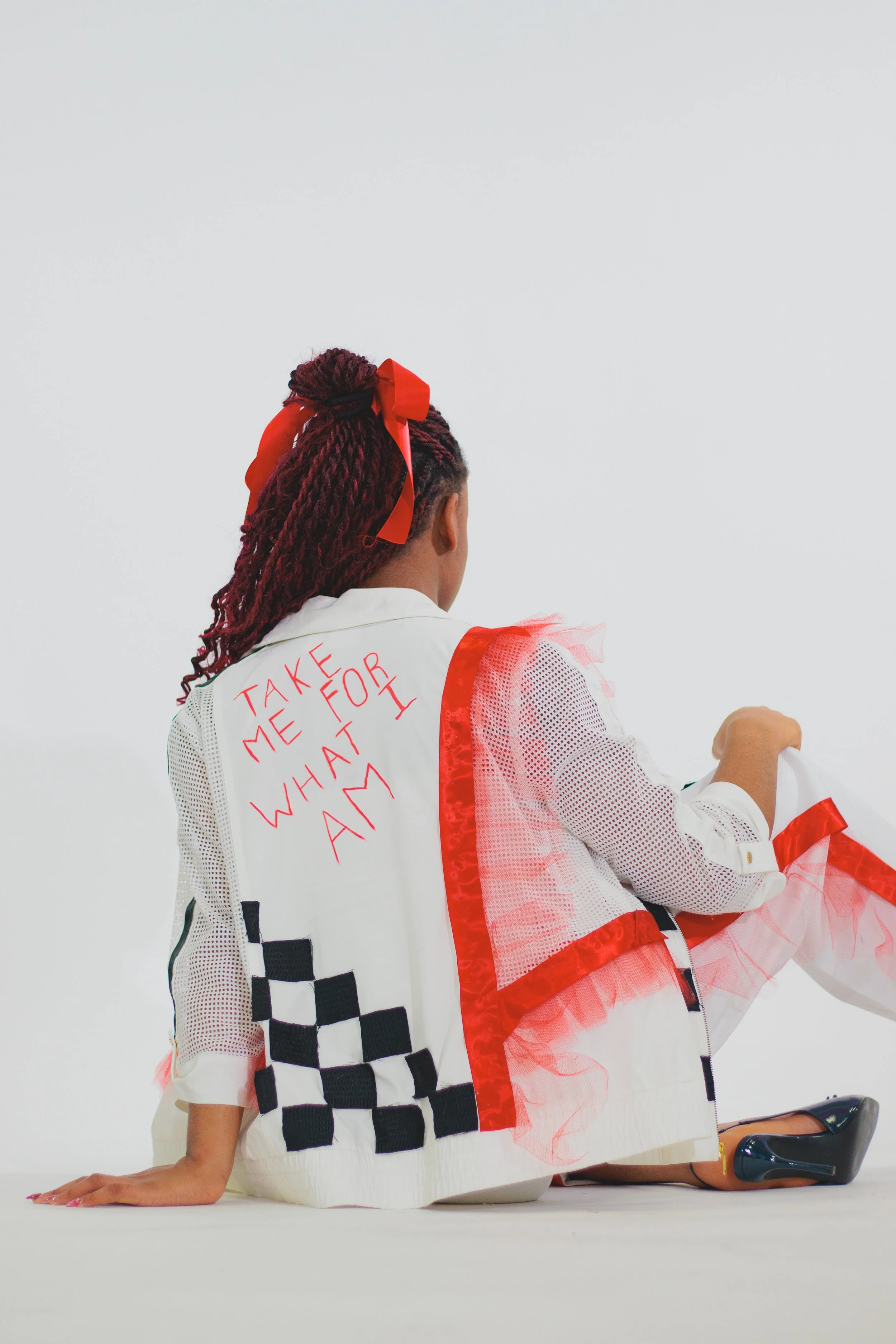 Woman in a white-and-red patriotic costume with a large red bow and braided hair, kneeling on the floor.