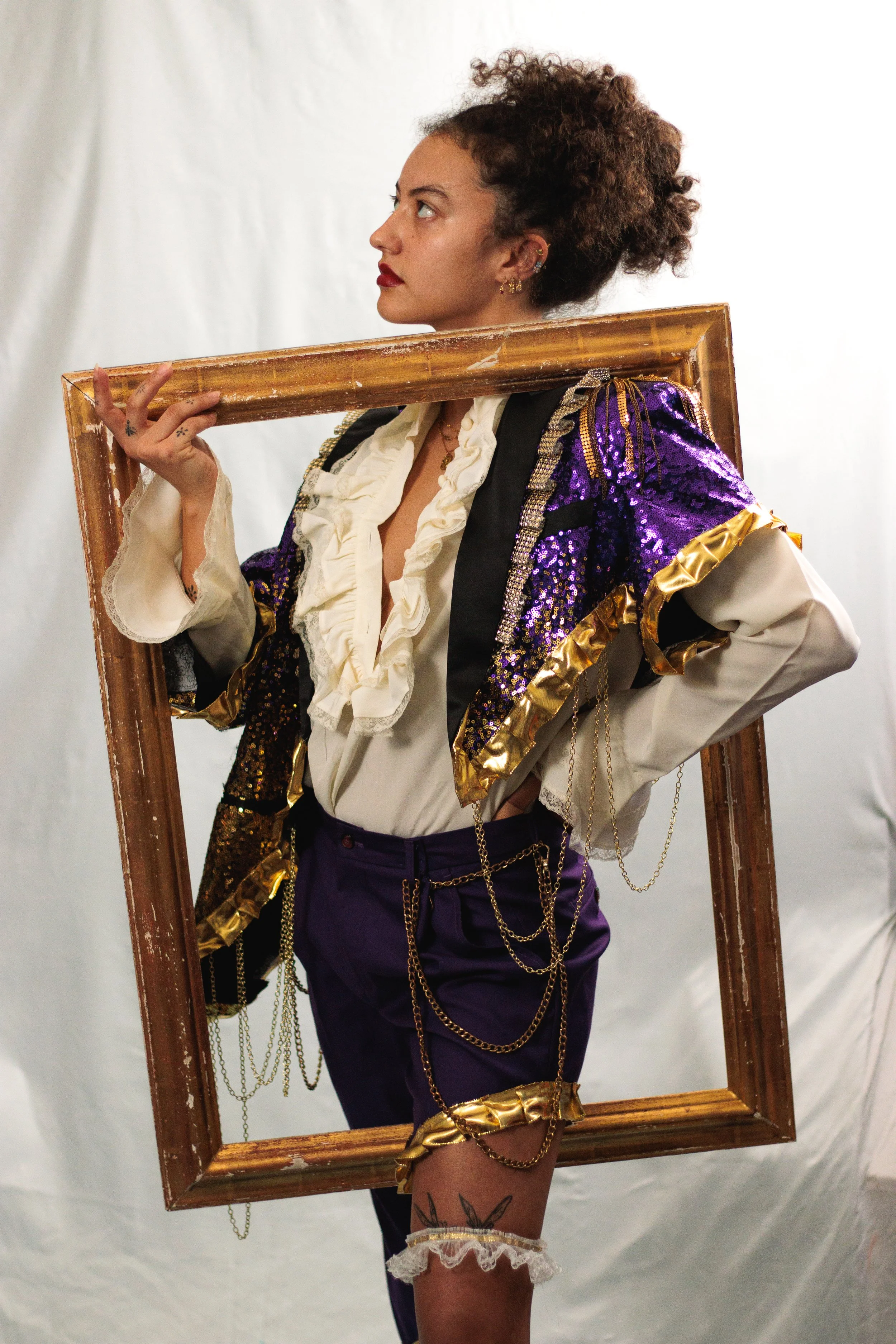 Person in a purple sequined costume and ruffled blouse posing inside a worn gold picture frame.