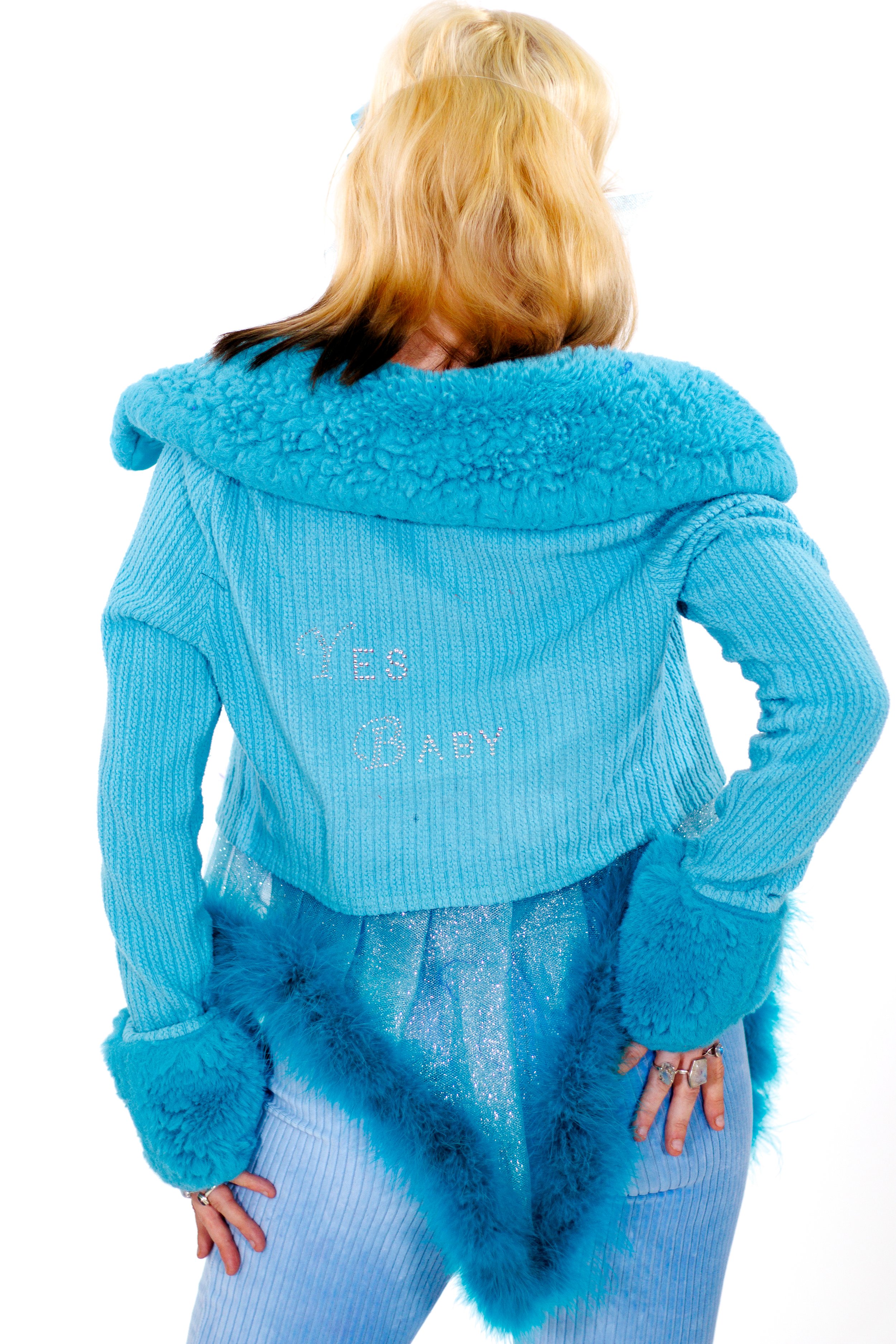 Person wearing a bright blue textured sweater with a faux-fur collar and glittering tulle skirt