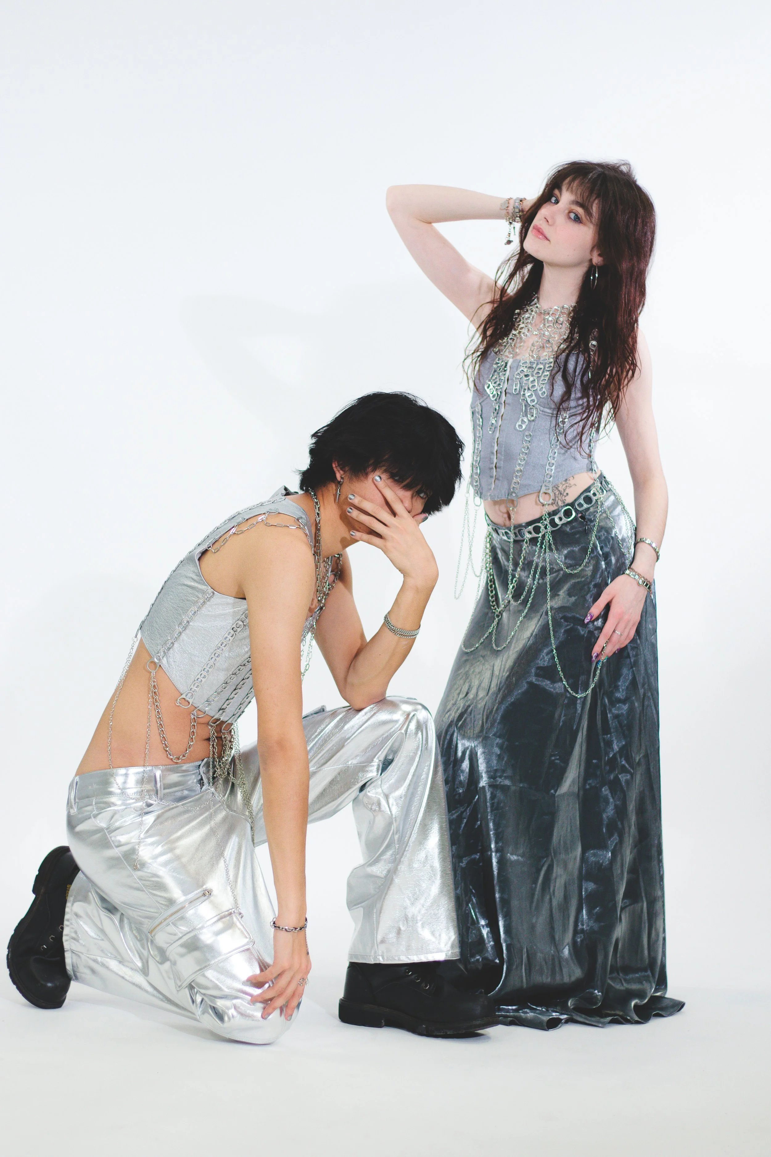 Two fashion models in metallic silver and black outfits posing against a white studio background