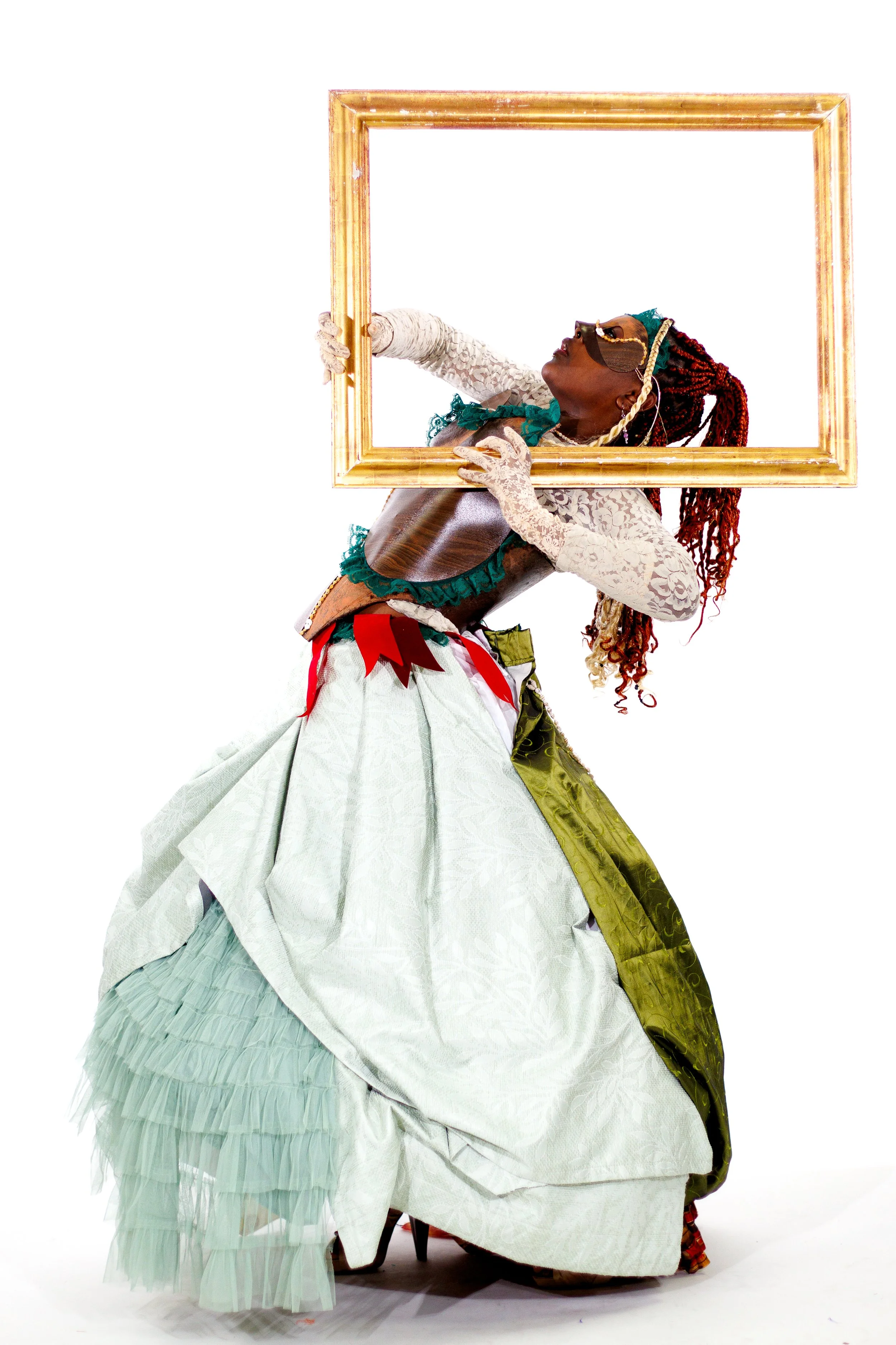 Black woman in an elaborate white lace costume posing behind an ornate gold picture frame