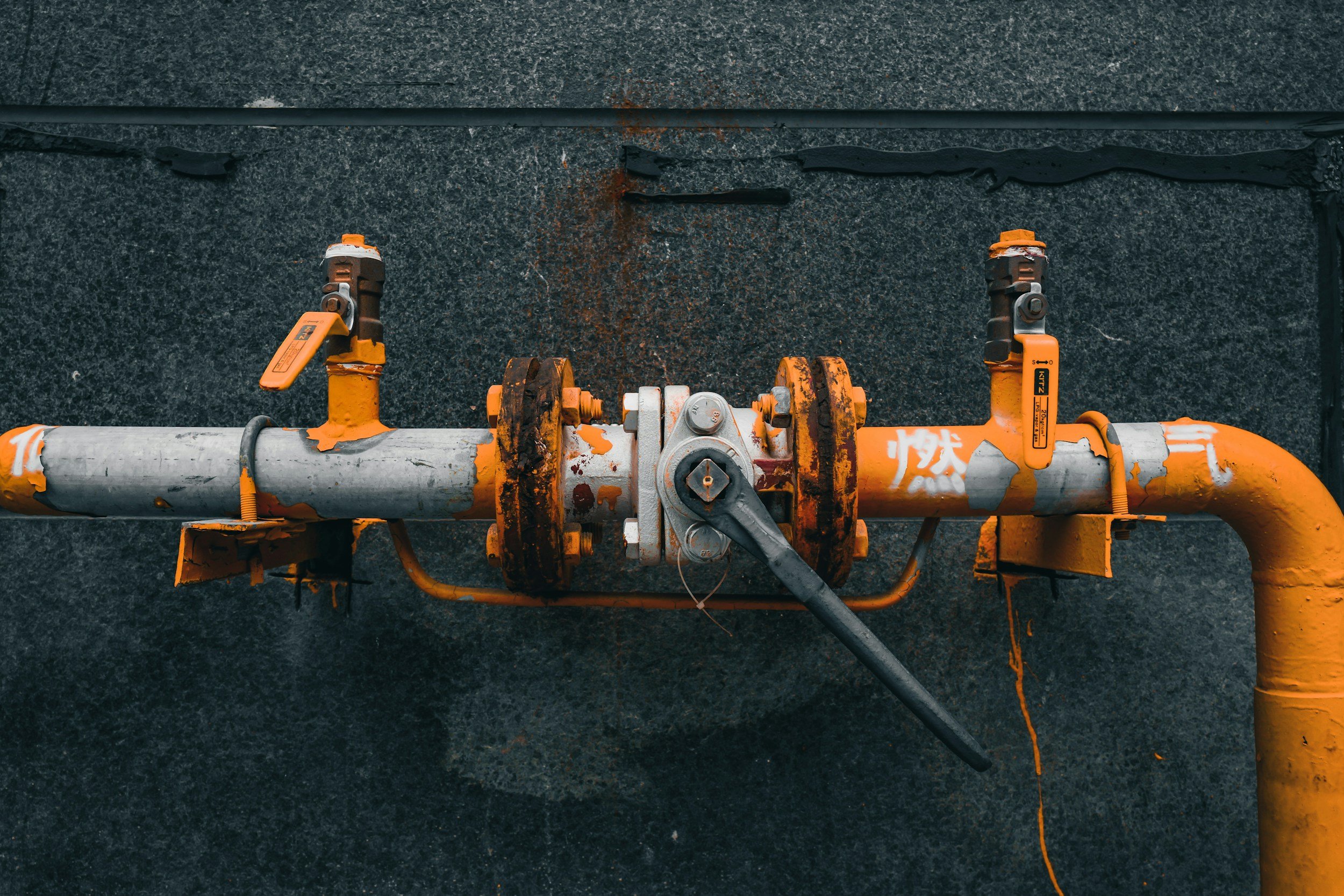 Close-up of a yellow industrial pipe with valves mounted on a rough black asphalt surface.