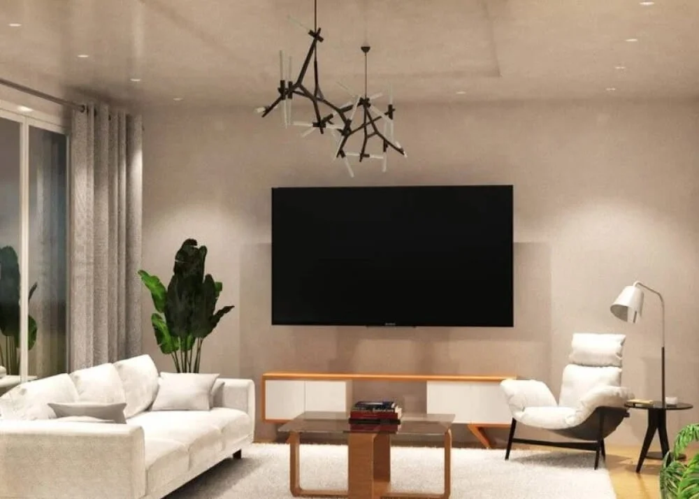 Modern living room with a white sofa, a large flat-screen TV on the wall, a white armchair with a floor lamp, a wooden coffee table, plants, and a chandelier.