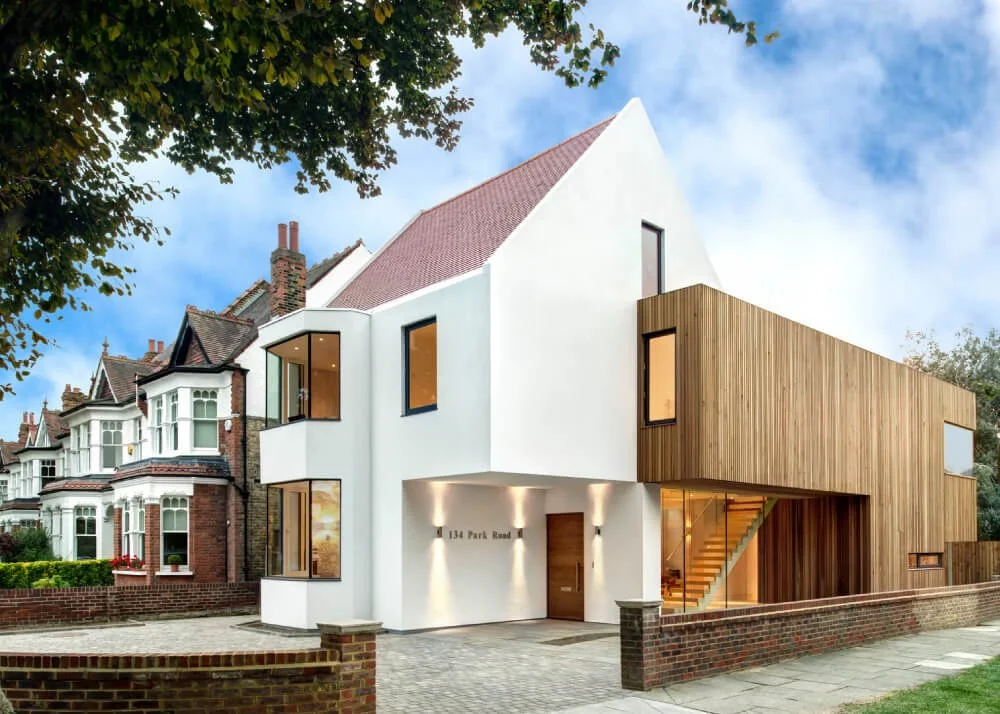 Modern house with white and wooden exterior, large windows, and a brick driveway, located on a residential street.