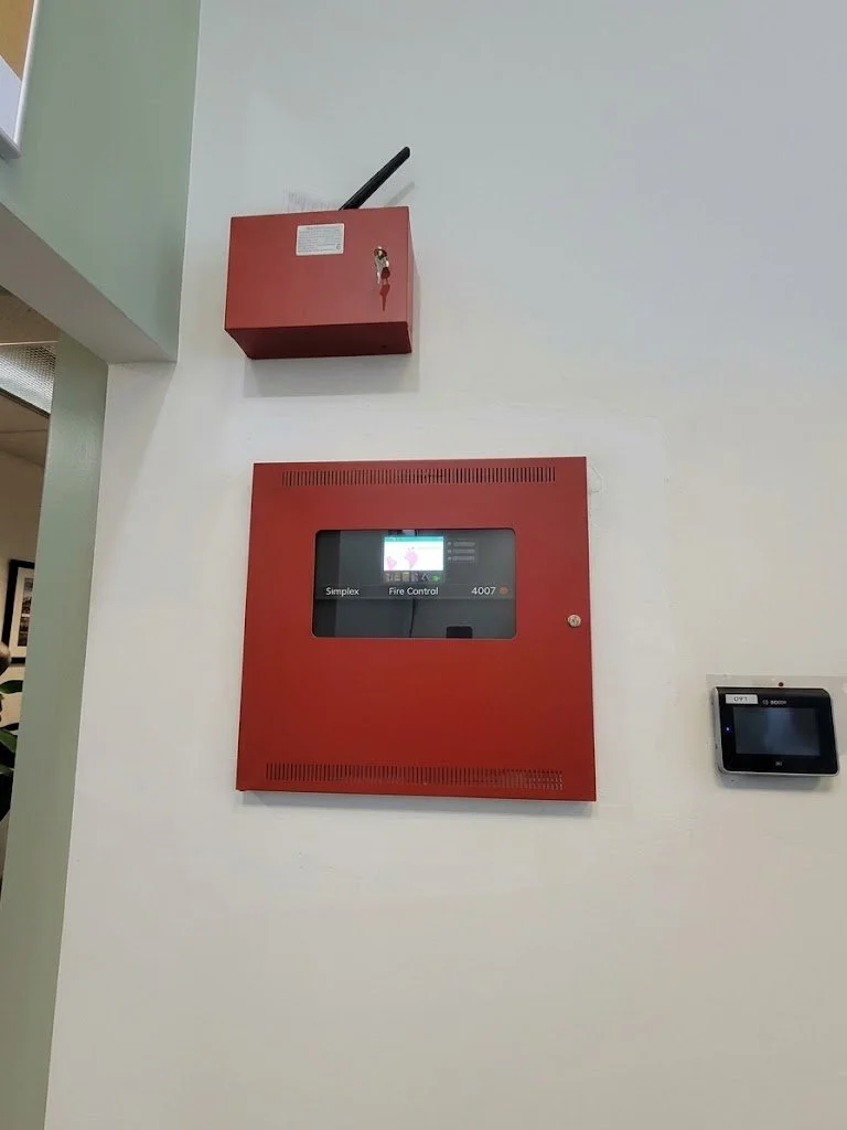 Red fire alarm control panel and a fire alarm box mounted on a white wall in a building.