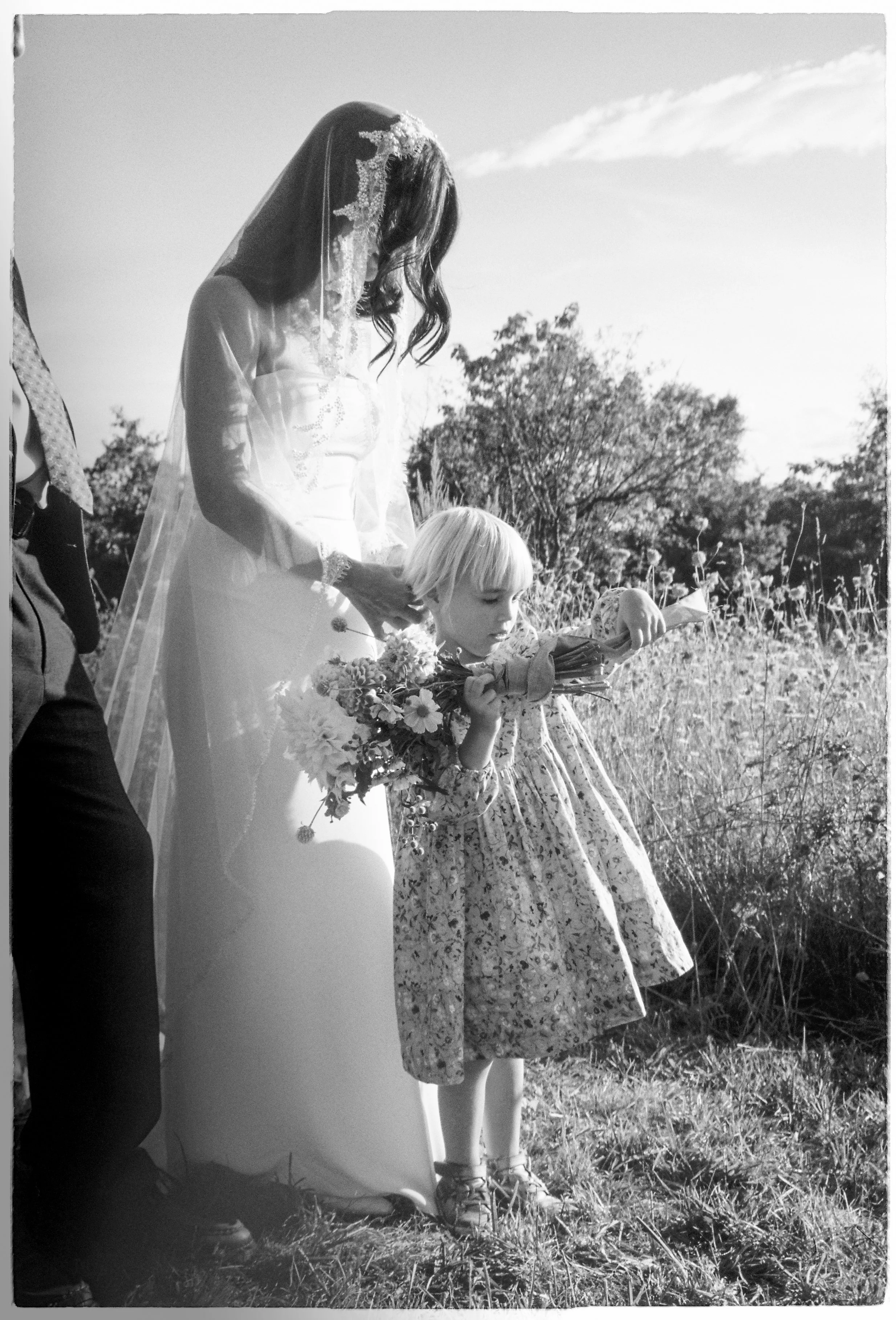 A bride on her wedding day holding a young girl's hair who is playing with the bride's bouquet.