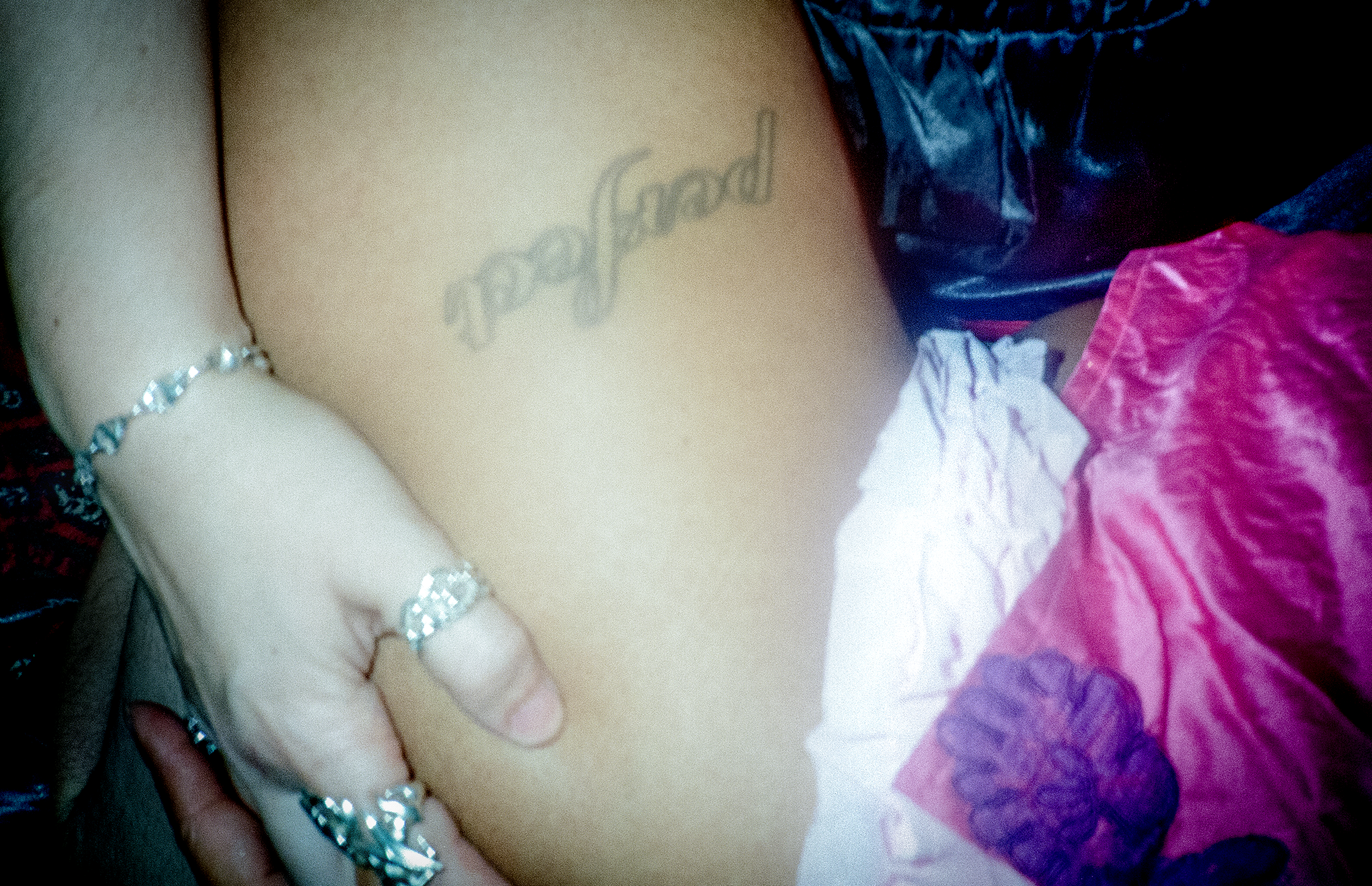 Close-up of a person's chest with a tattoo and jewelry visible, wearing a purple top and a bracelet.