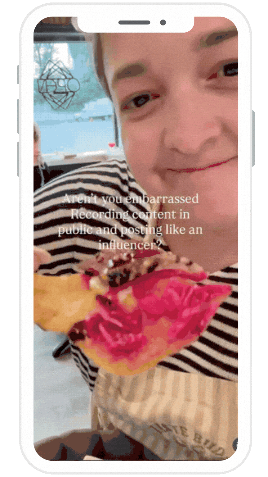 Close-up of a smiling boy wearing a black and white striped shirt, holding a slice of watermelon with pink flesh and dark seeds. The background shows a window with water outside and a decorative wall hanging.