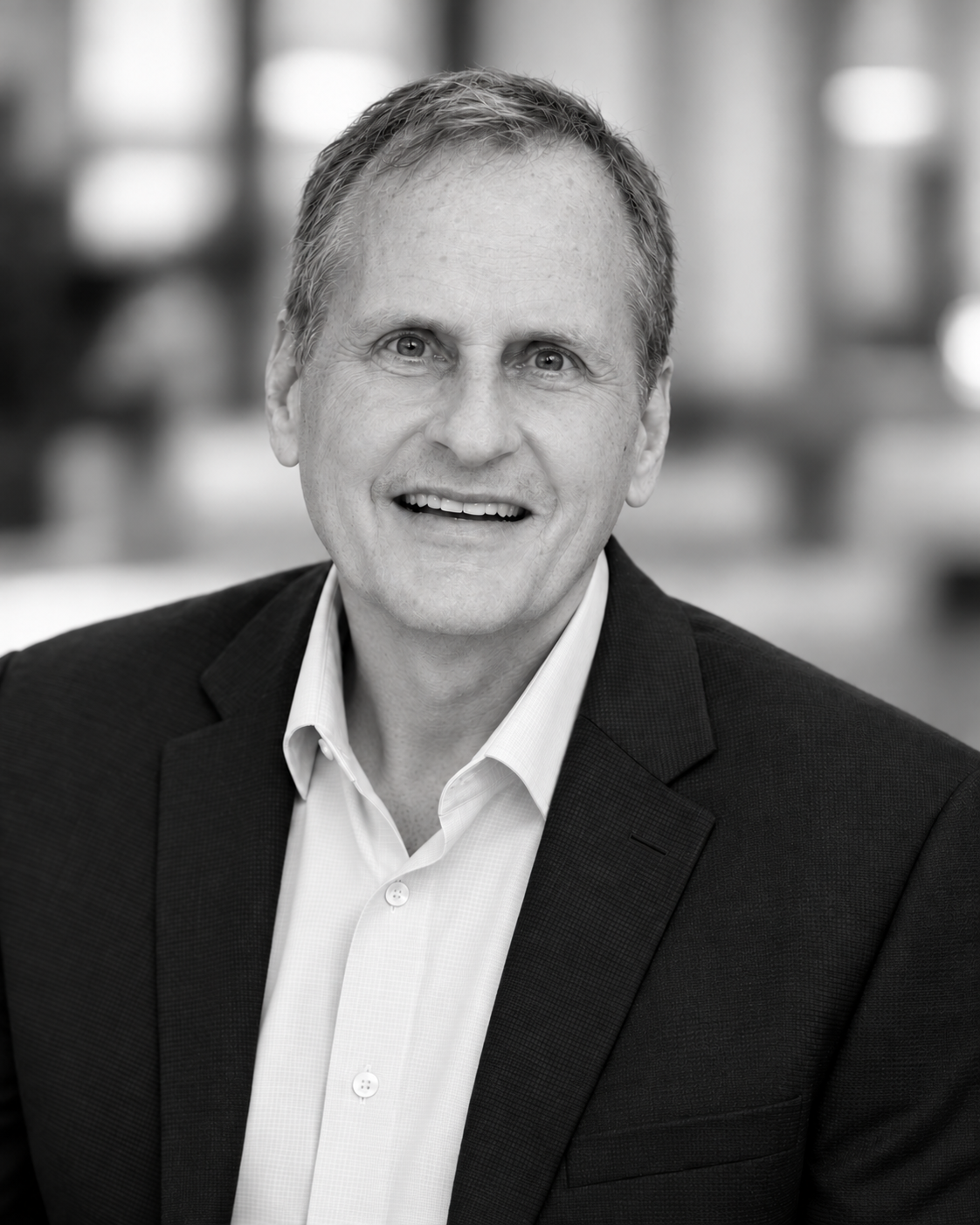 Black and white portrait of a smiling middle-aged man in a suit, with a blurred indoor background.