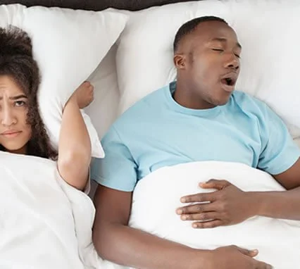 Man snoring in bed next to his partner