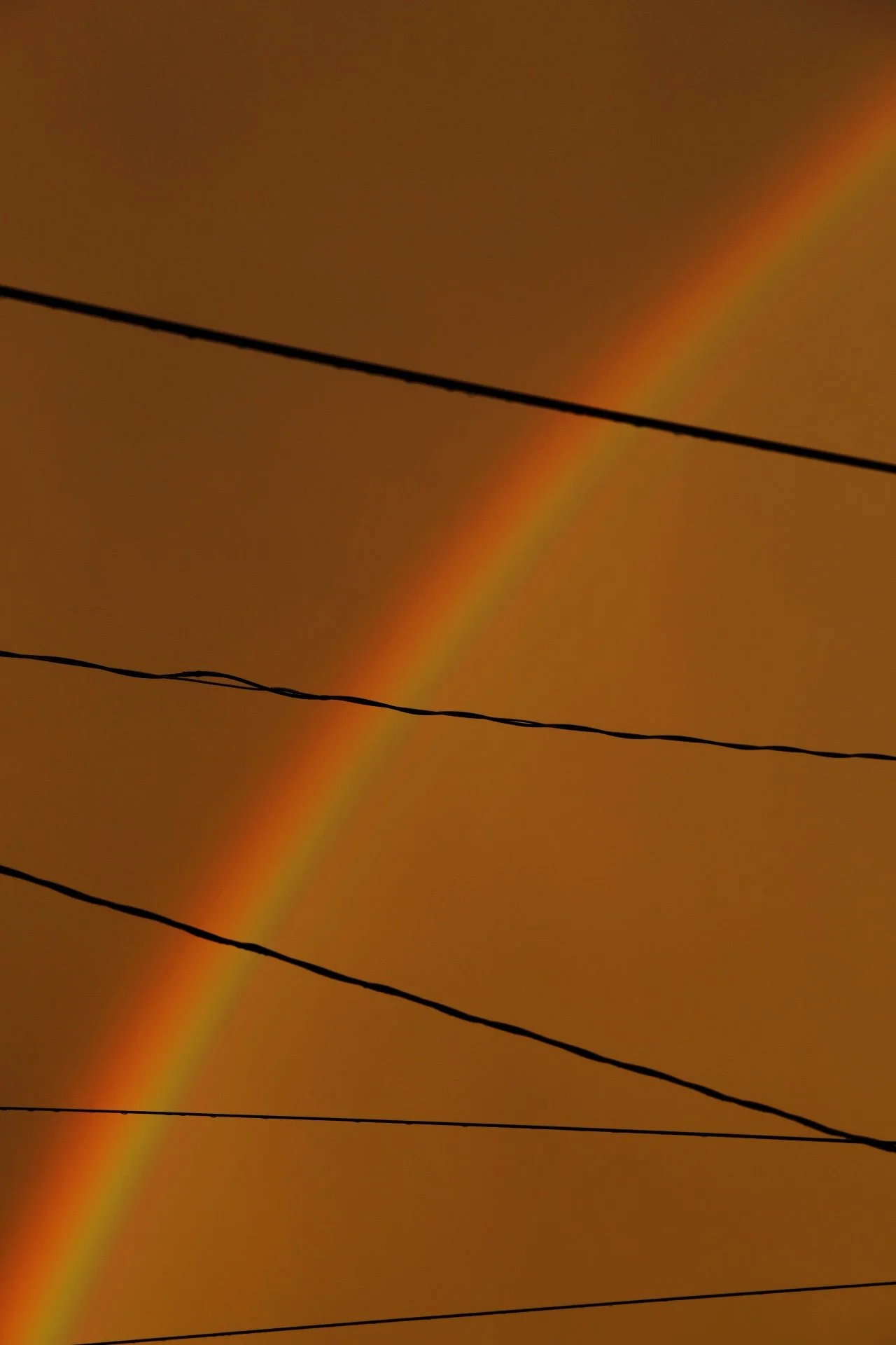 A faint rainbow arching across a cloudy sky with power lines in the foreground.