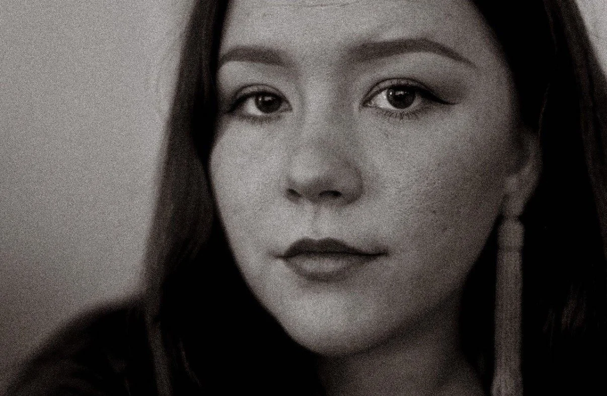 Black and white close-up portrait of a woman with dark hair, eyeliner, and a confident expression.