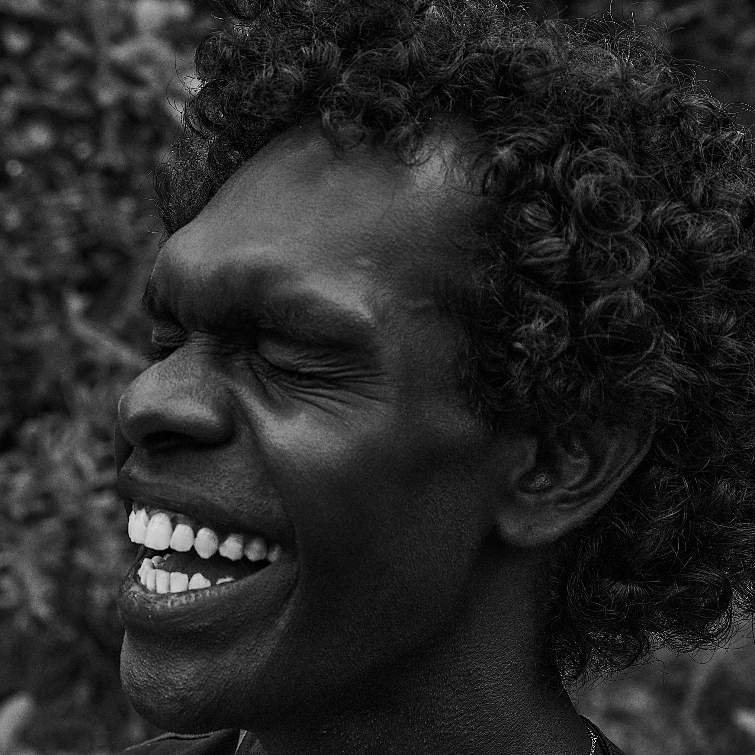 Black-and-white close-up portrait of Jack Minmidi, a Yolŋu man from Milingimbi, smiling with his eyes closed.