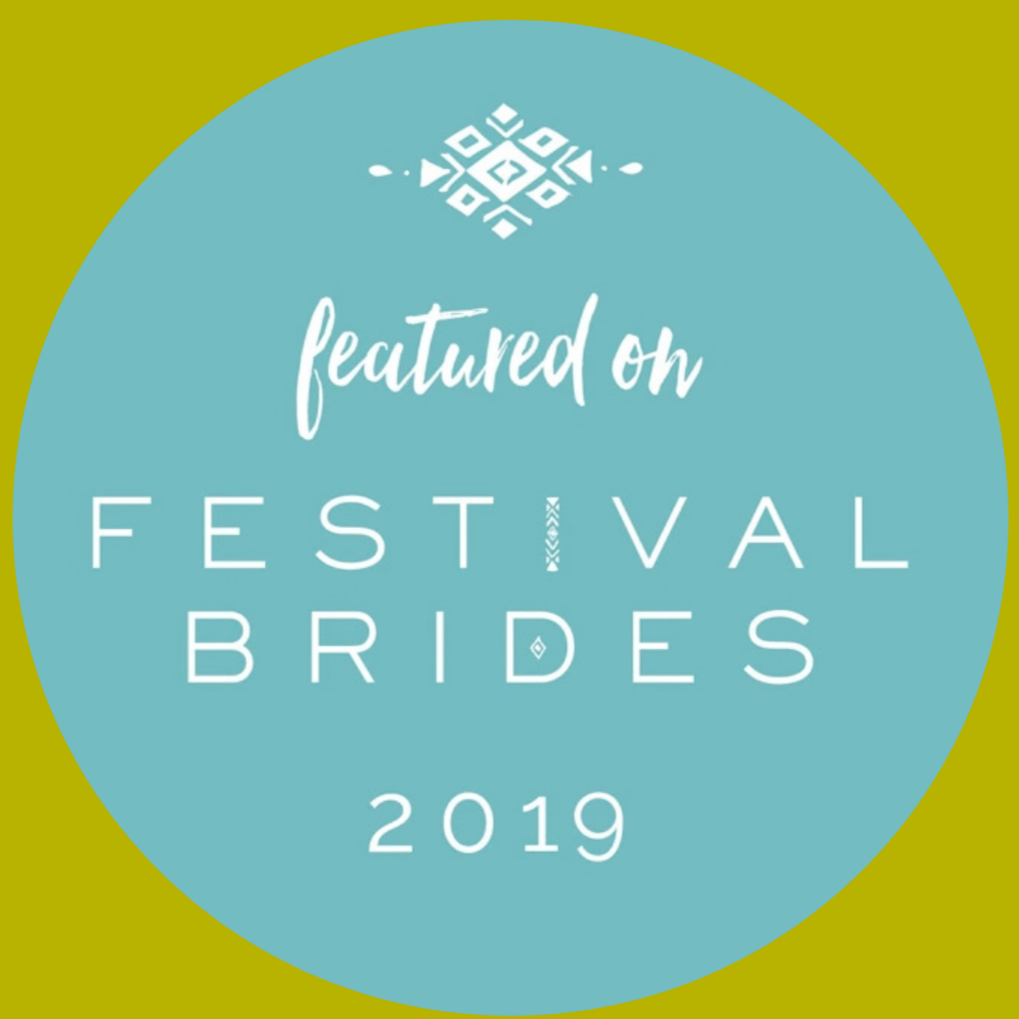 Blue circular badge with white text and a decorative element at the top. The badge reads, 'featured on FESTIVAL BRIDES 2019.'