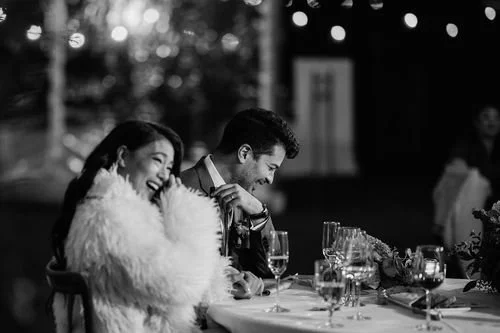 A couple smiling and laughing at a table during a celebration or wedding reception.